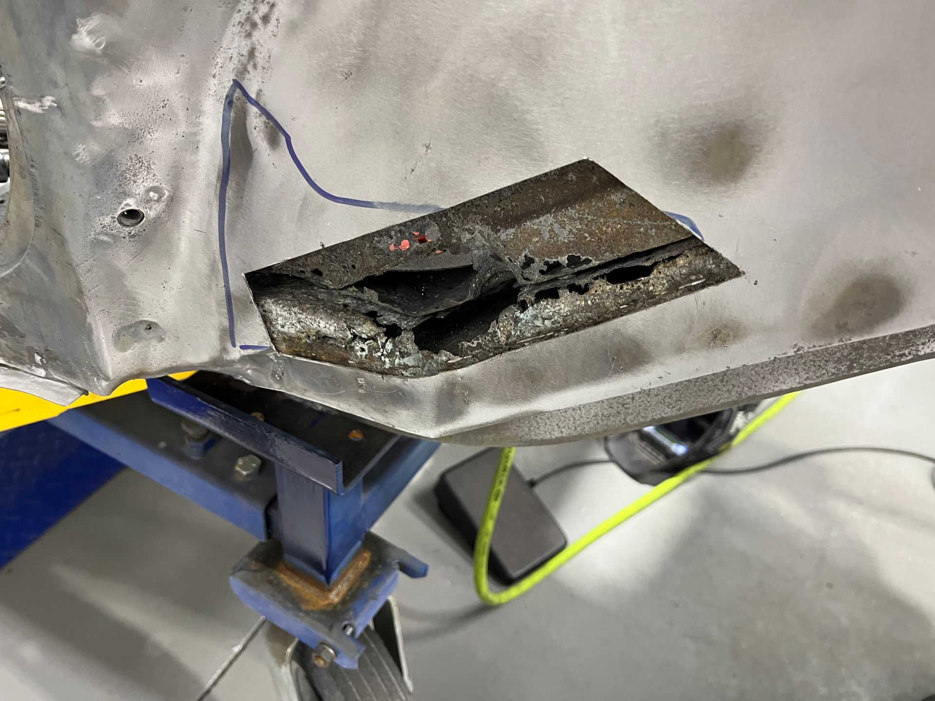 Damaged gray metal panel with a torn opening, supported by a blue stand in a workshop setting