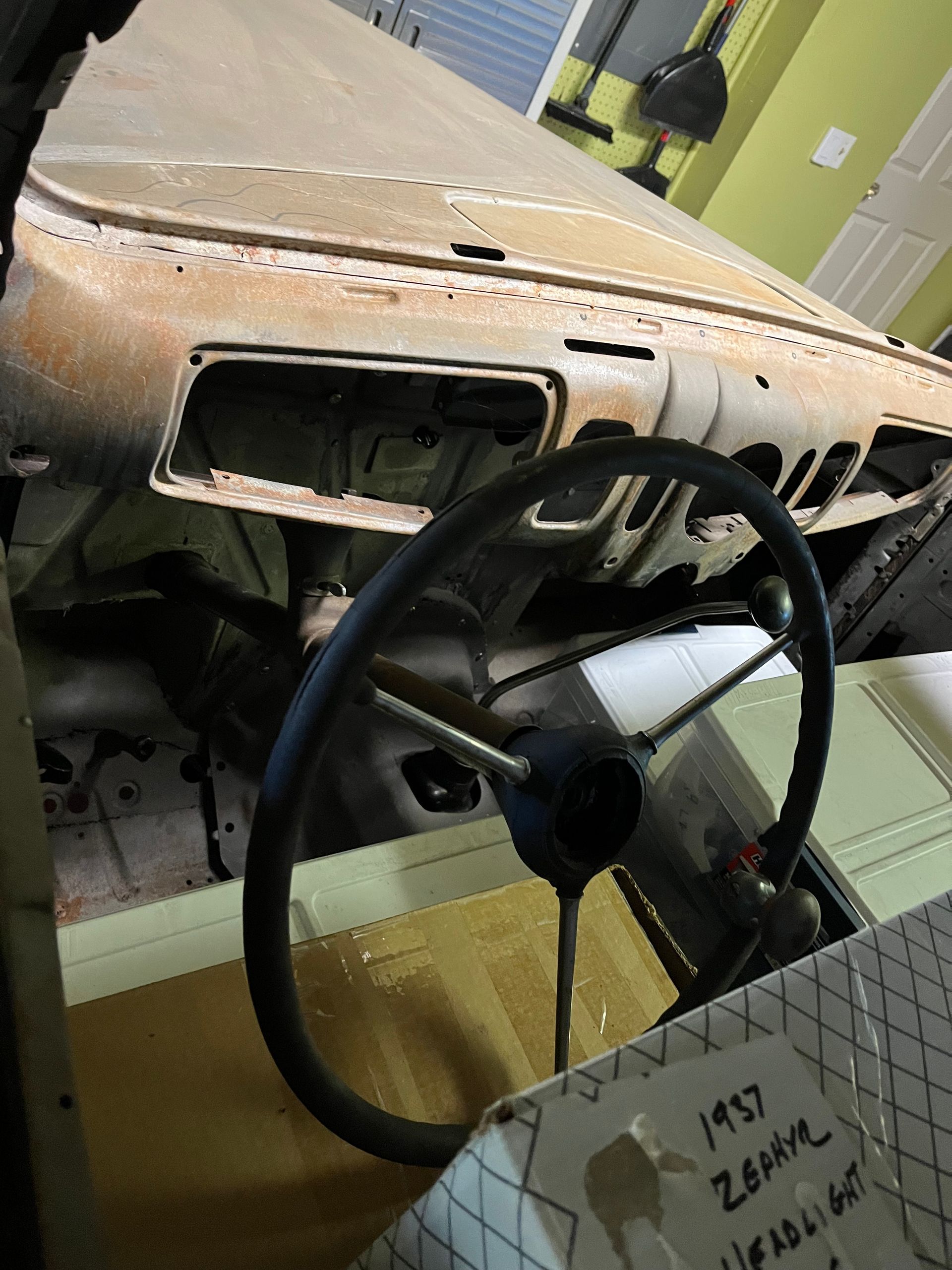 Abandoned car interior with a black steering wheel and stripped dashboard, rusted and unfinished.