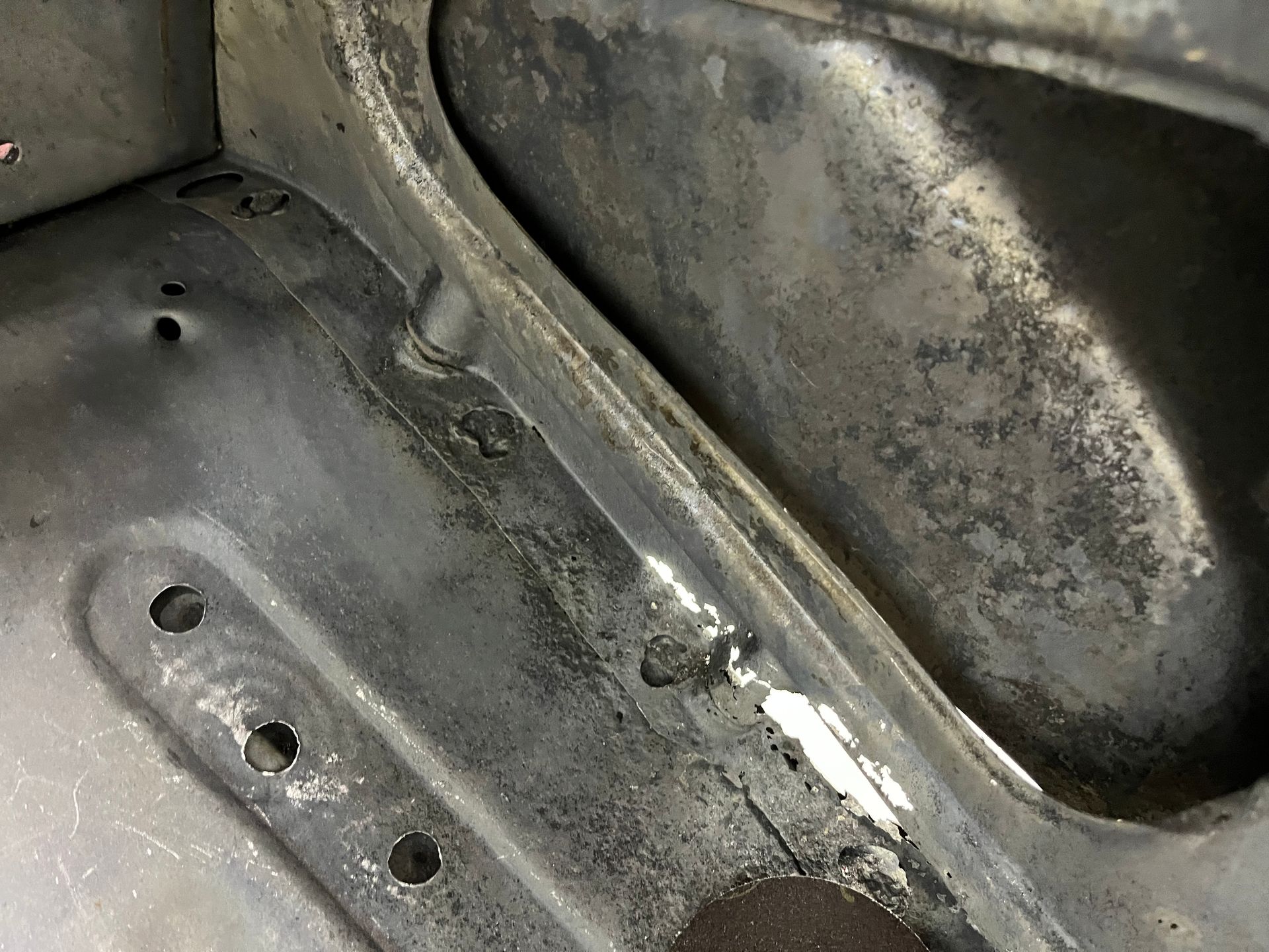 Close-up of a dirty, worn metal car interior panel with rust spots and holes