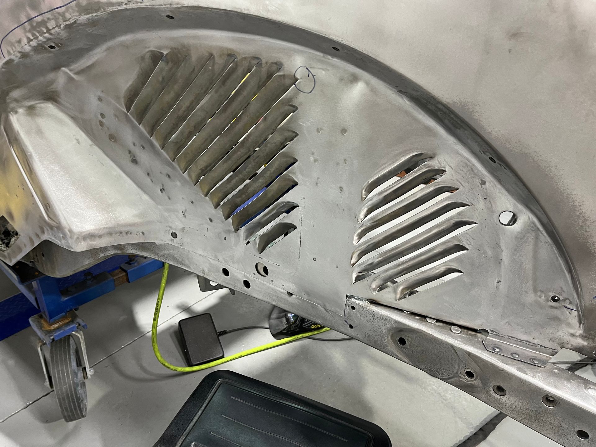Damaged silver car body panel with vent slats and sanding marks in a workshop
