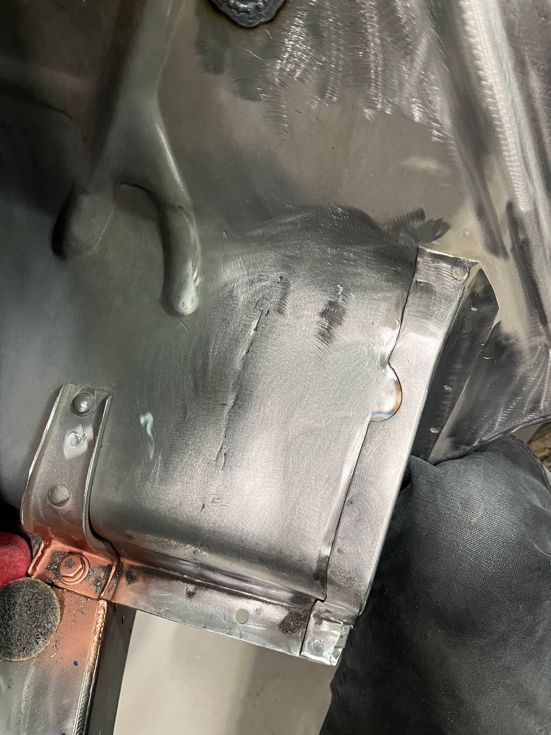 Close-up of a black metal part with a welded seam and a rusty bracket attached inside a vehicle or machinery.