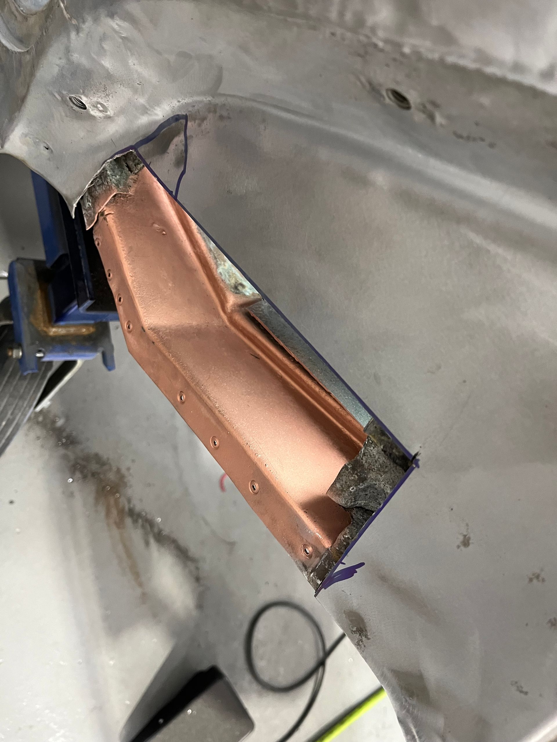 Copper-colored metal bracket attached to a gray structure, with a small black clip at the end.