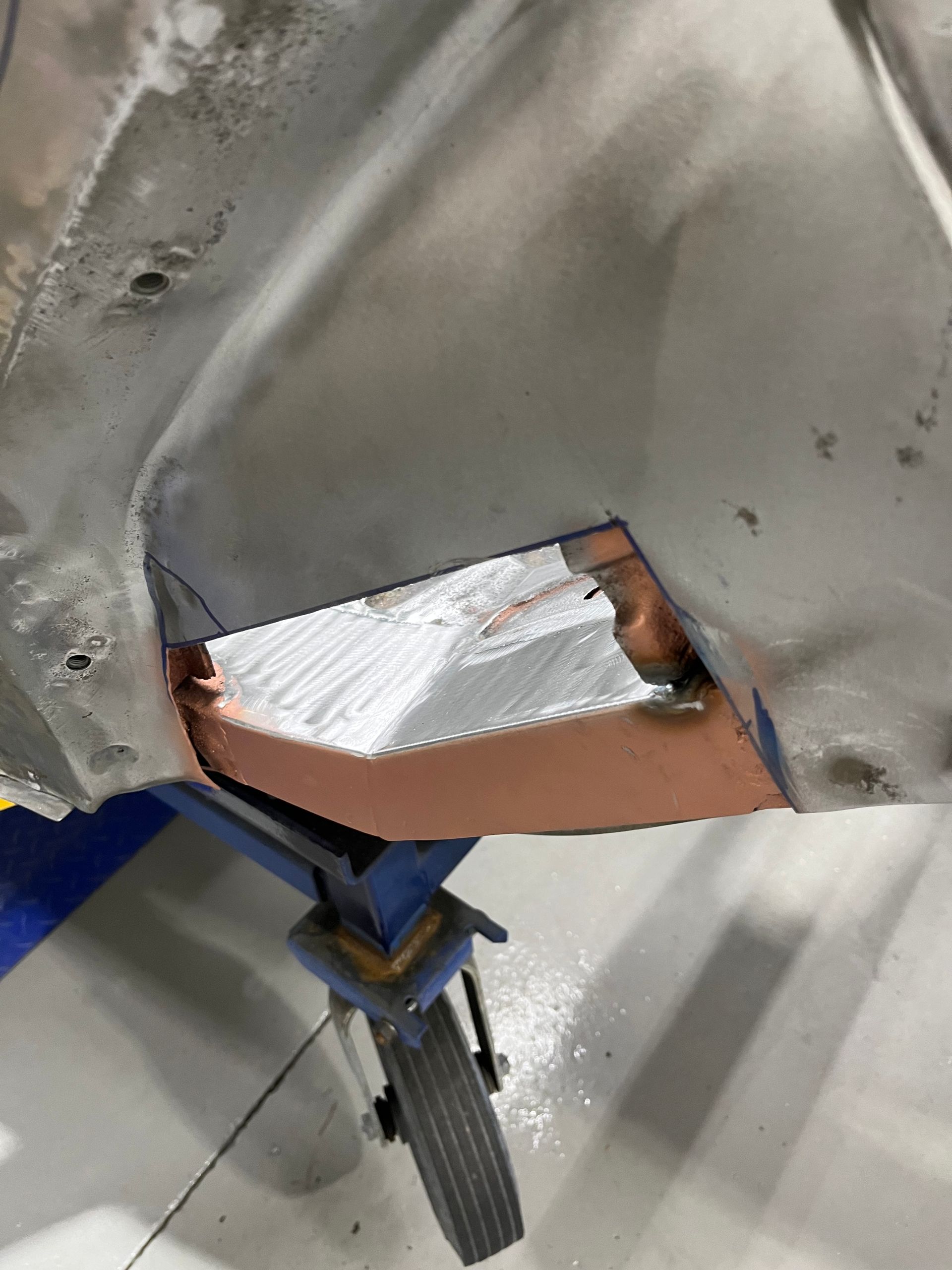 Close-up of damaged metal panel with torn white insulation and rust, above a wheel assembly