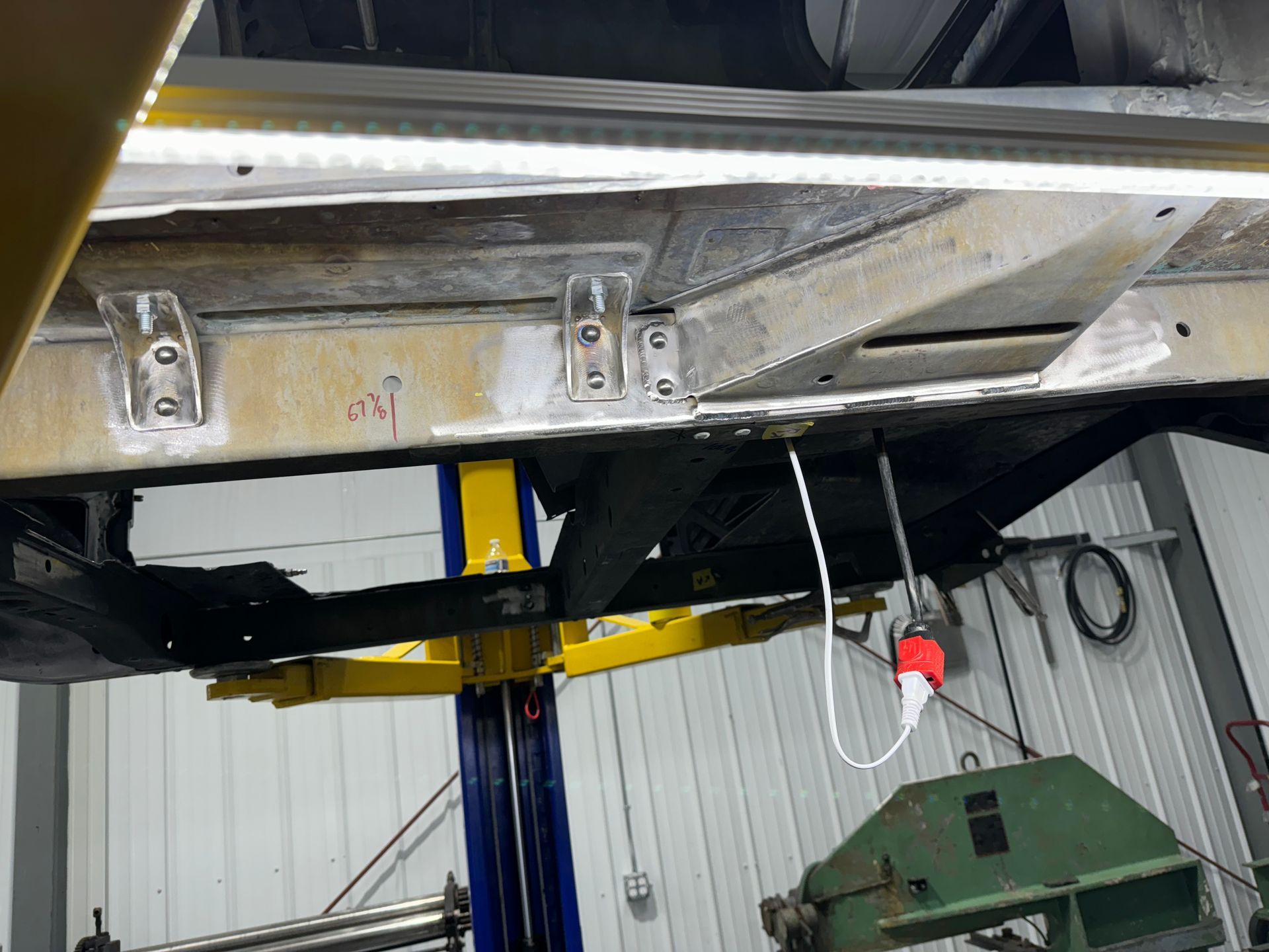 Underside of a vehicle on a lift in a garage, with metal framework and a hanging cord visible.