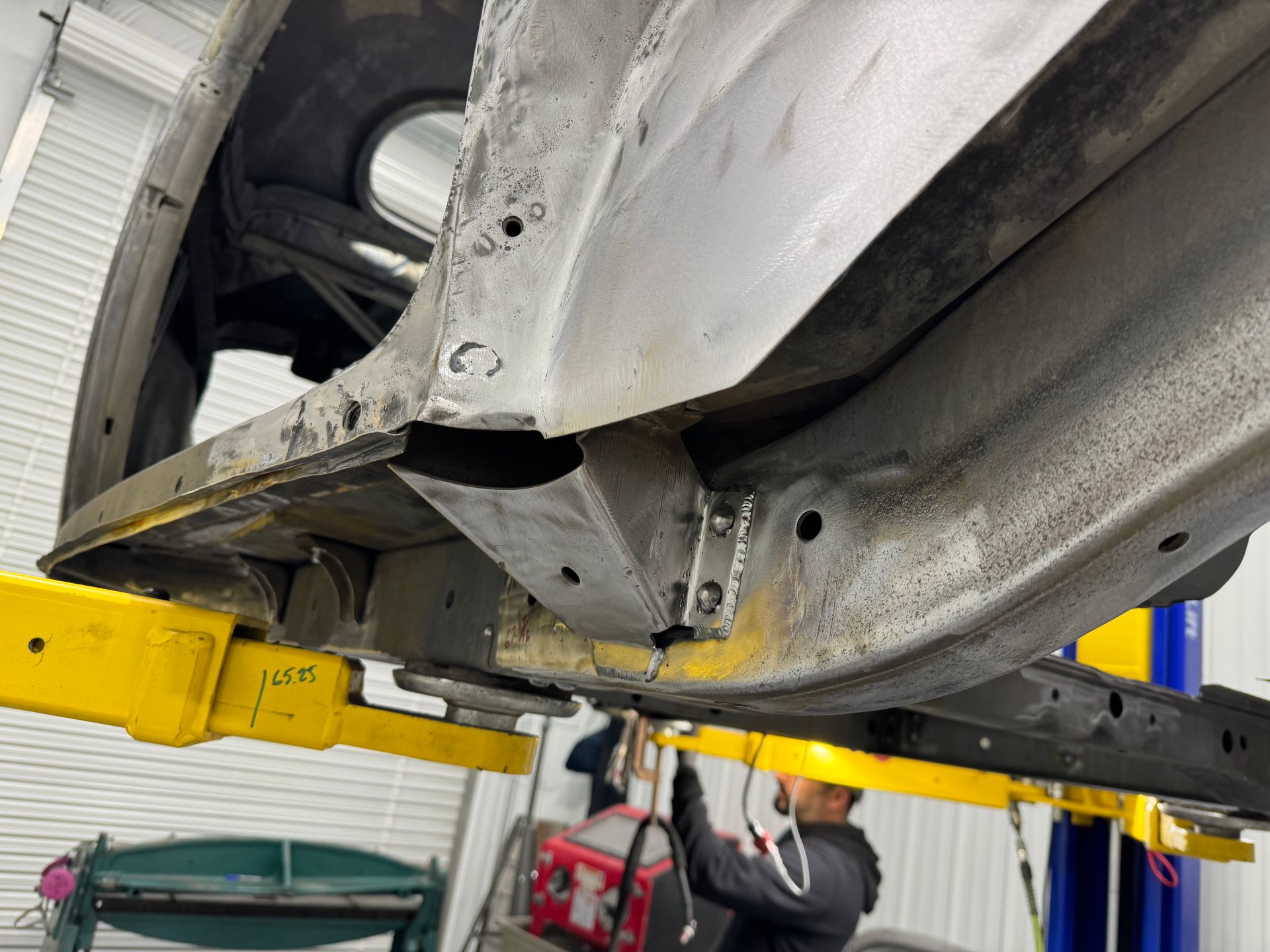 Undercarriage of a white car lifted on a yellow hydraulic lift in a repair shop