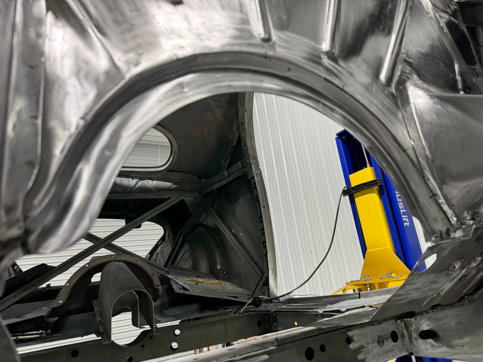 Inside a car body shell, a mechanic works near the rear frame in a workshop