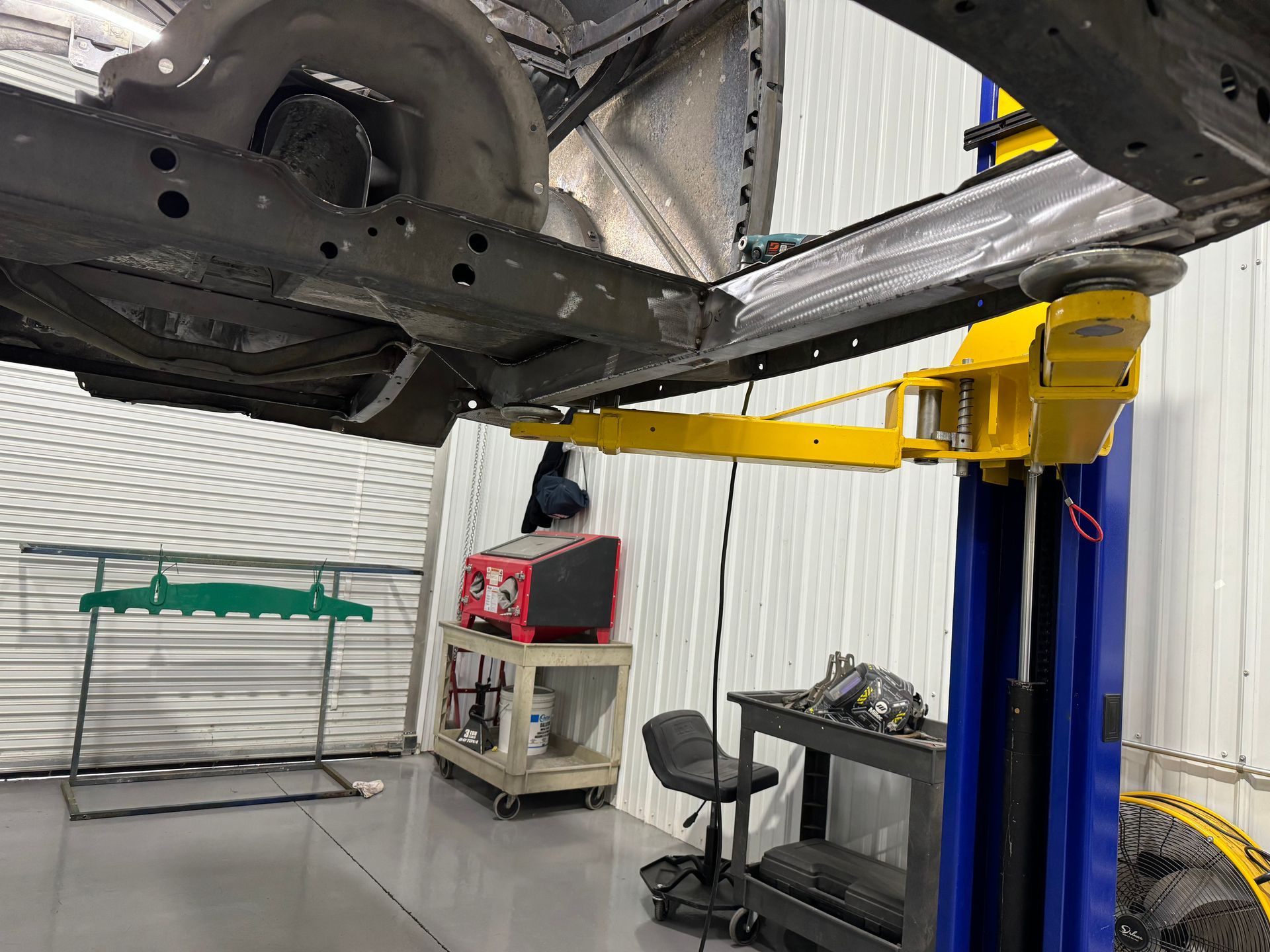 Car lift holding a vehicle in a garage, with a person at a workbench and tools nearby.