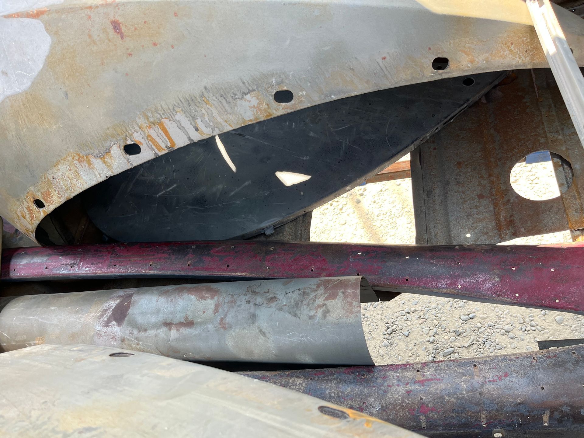Close-up of rusted metal undercarriage with pipes and a maroon bar in a dusty outdoor setting