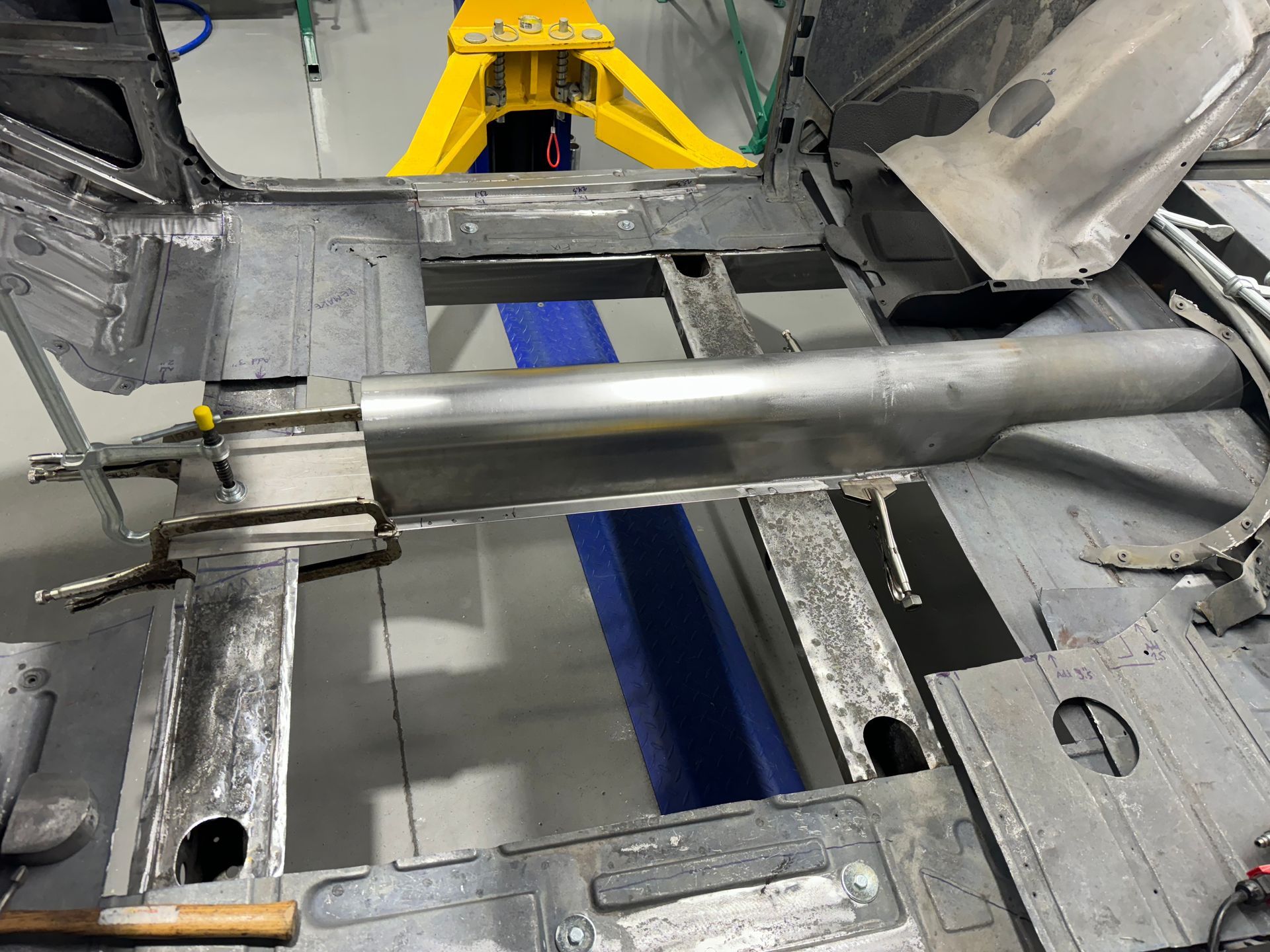 Silver metal rod mounted inside a gray machine frame with yellow machinery in the background