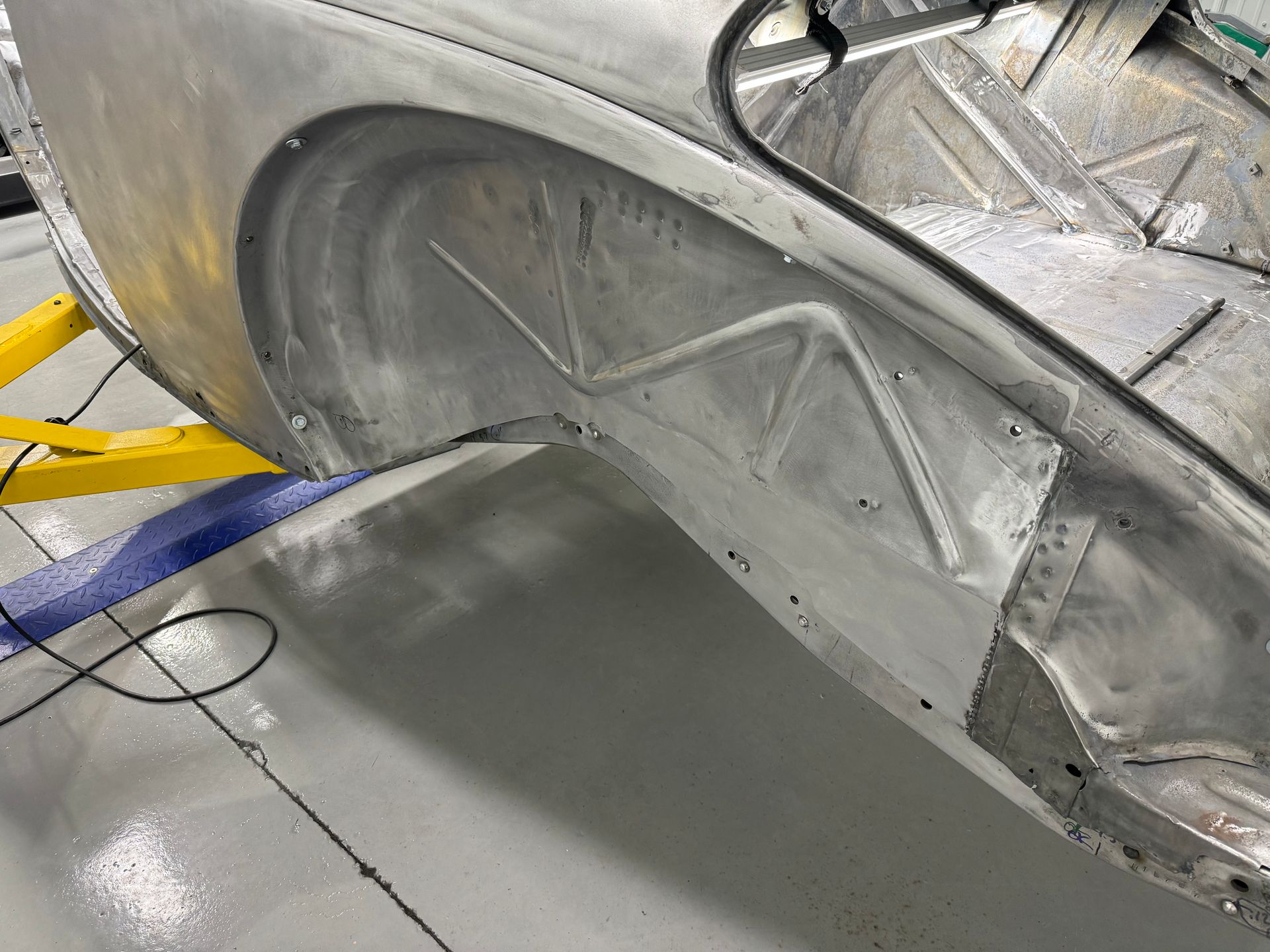 Close-up of a silver car body panel and wheel well under repair in a workshop
