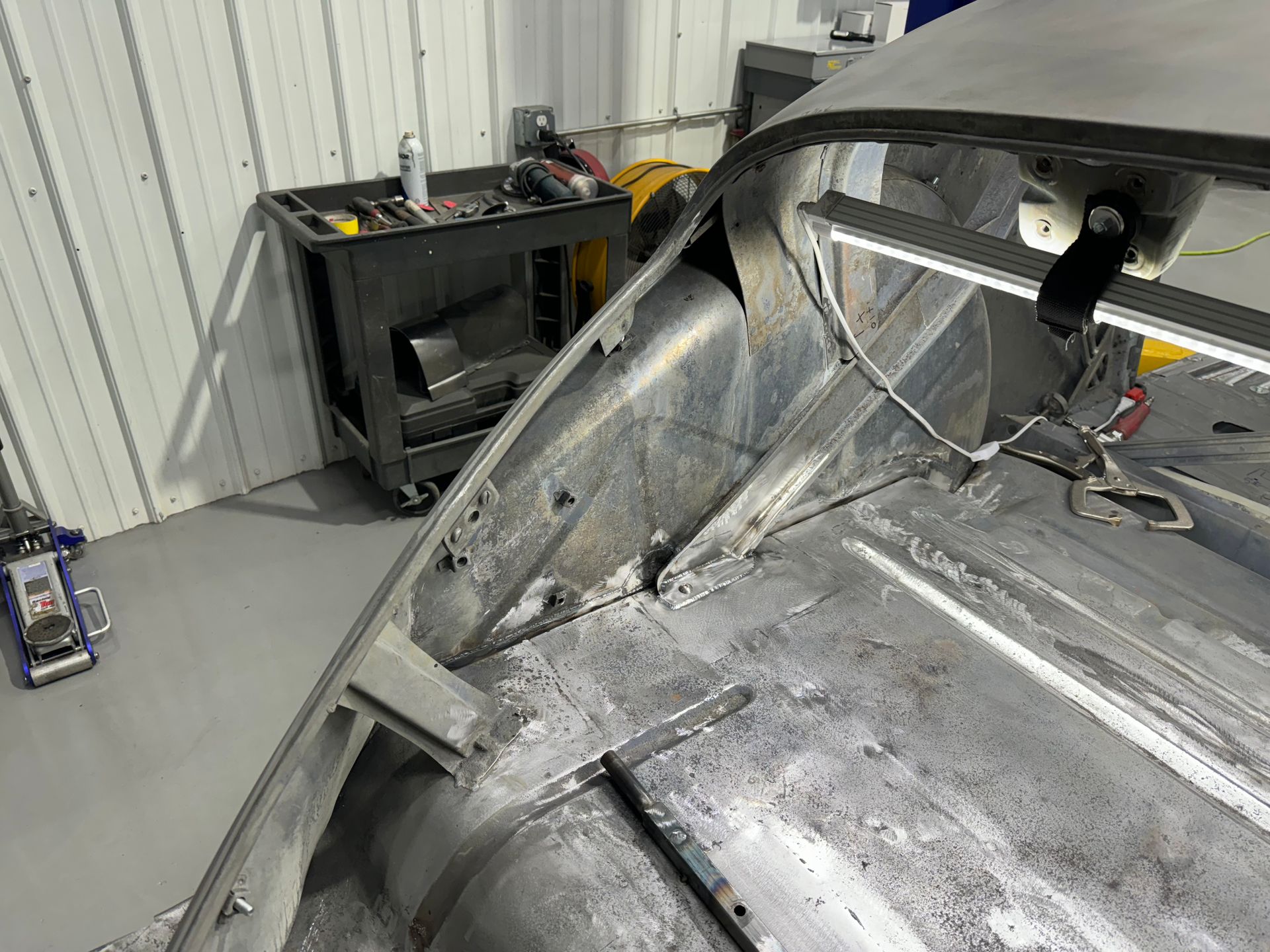 Damaged gray car body in a workshop, with exposed metal and tools in the background