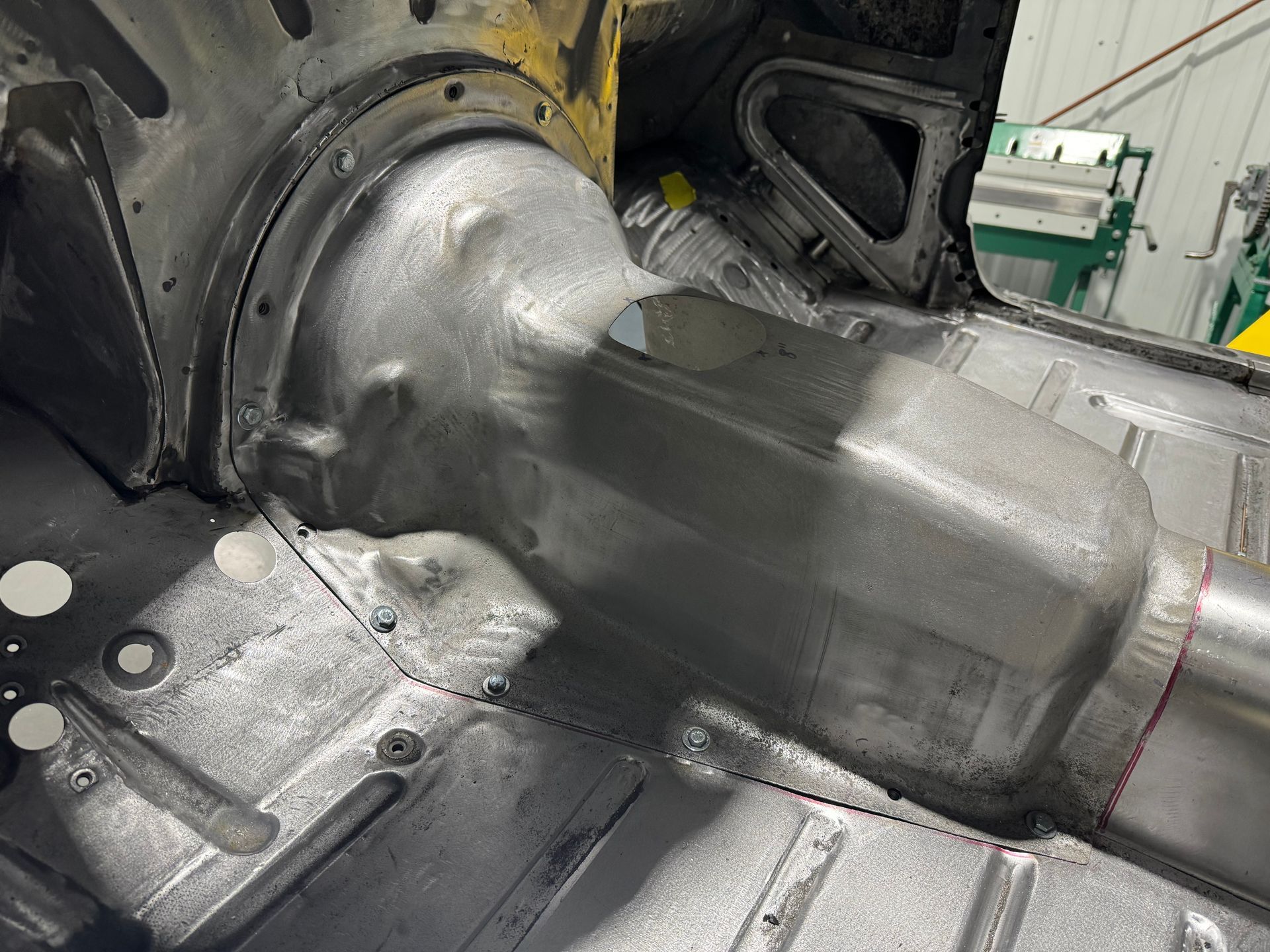 Shiny silver metal exhaust pipe welded to a car body in a workshop