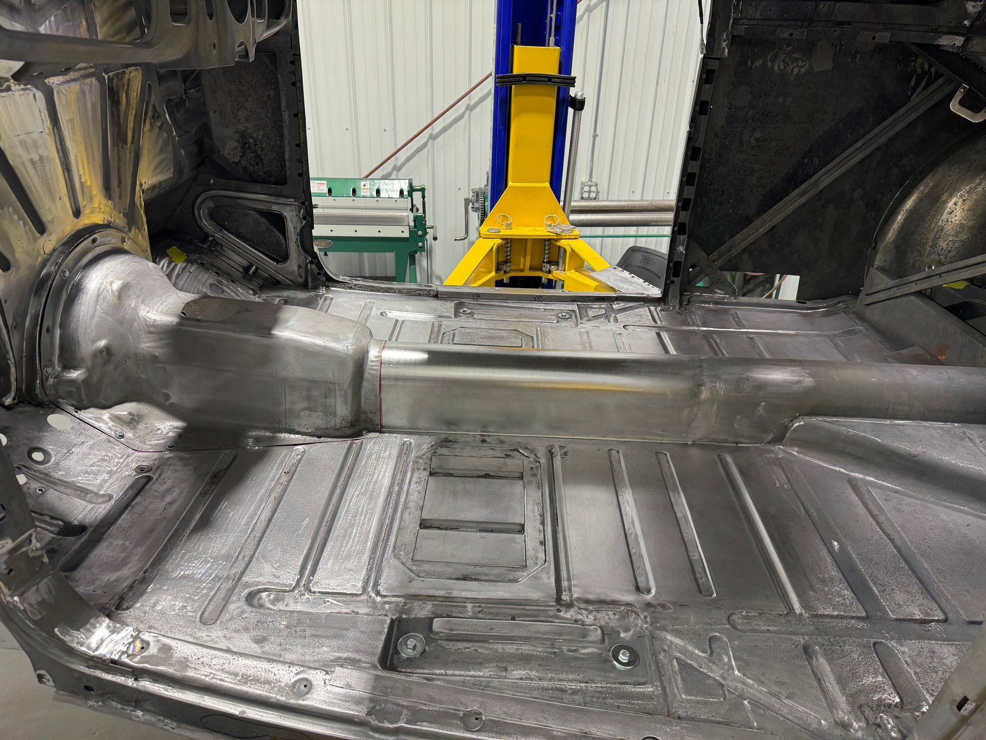 Damaged car undercarriage on a lift, showing a bent exhaust and exposed floor pan in a workshop