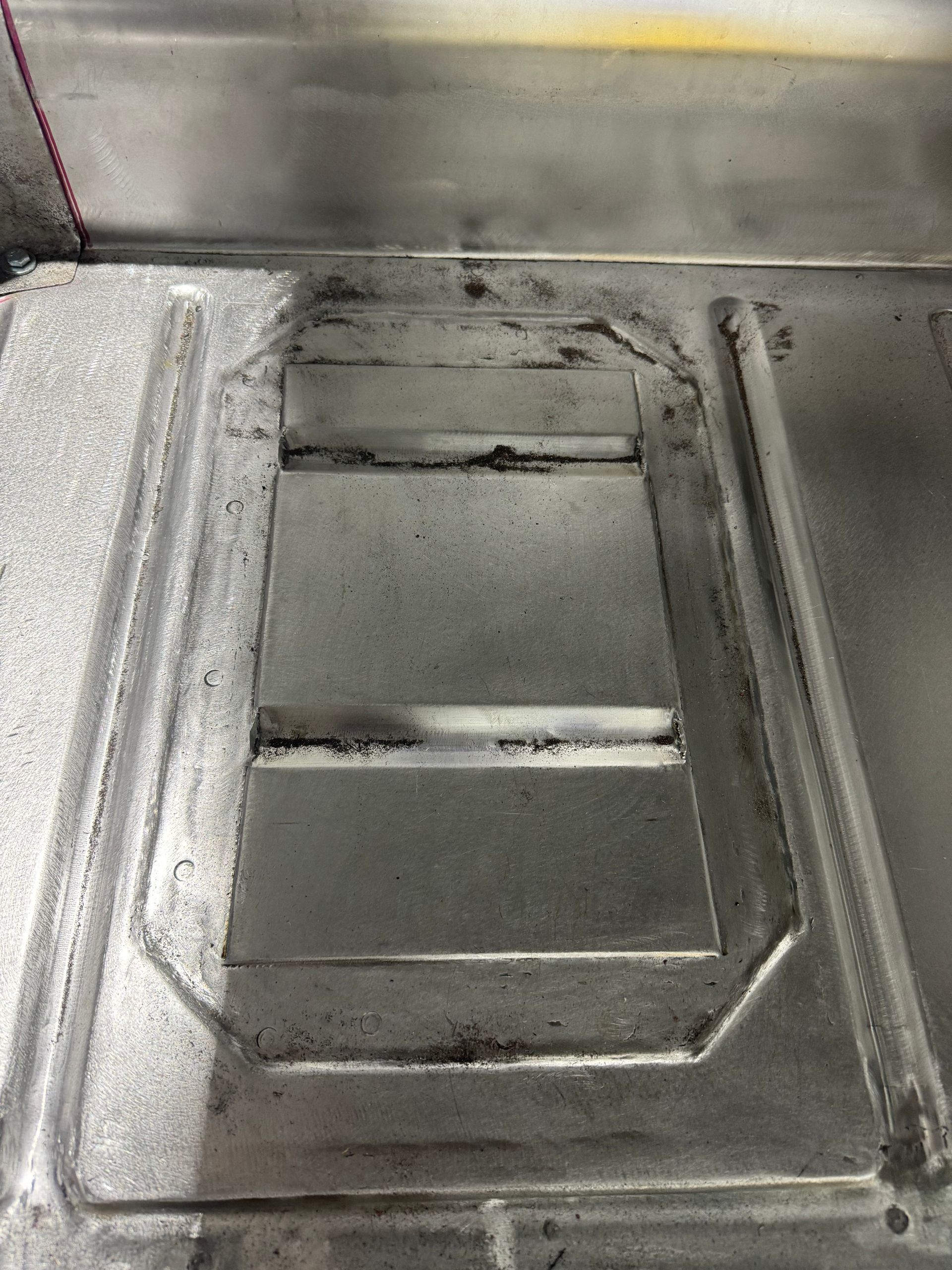 Close-up of a stainless steel sink basin with a rectangular drain and worn edges.