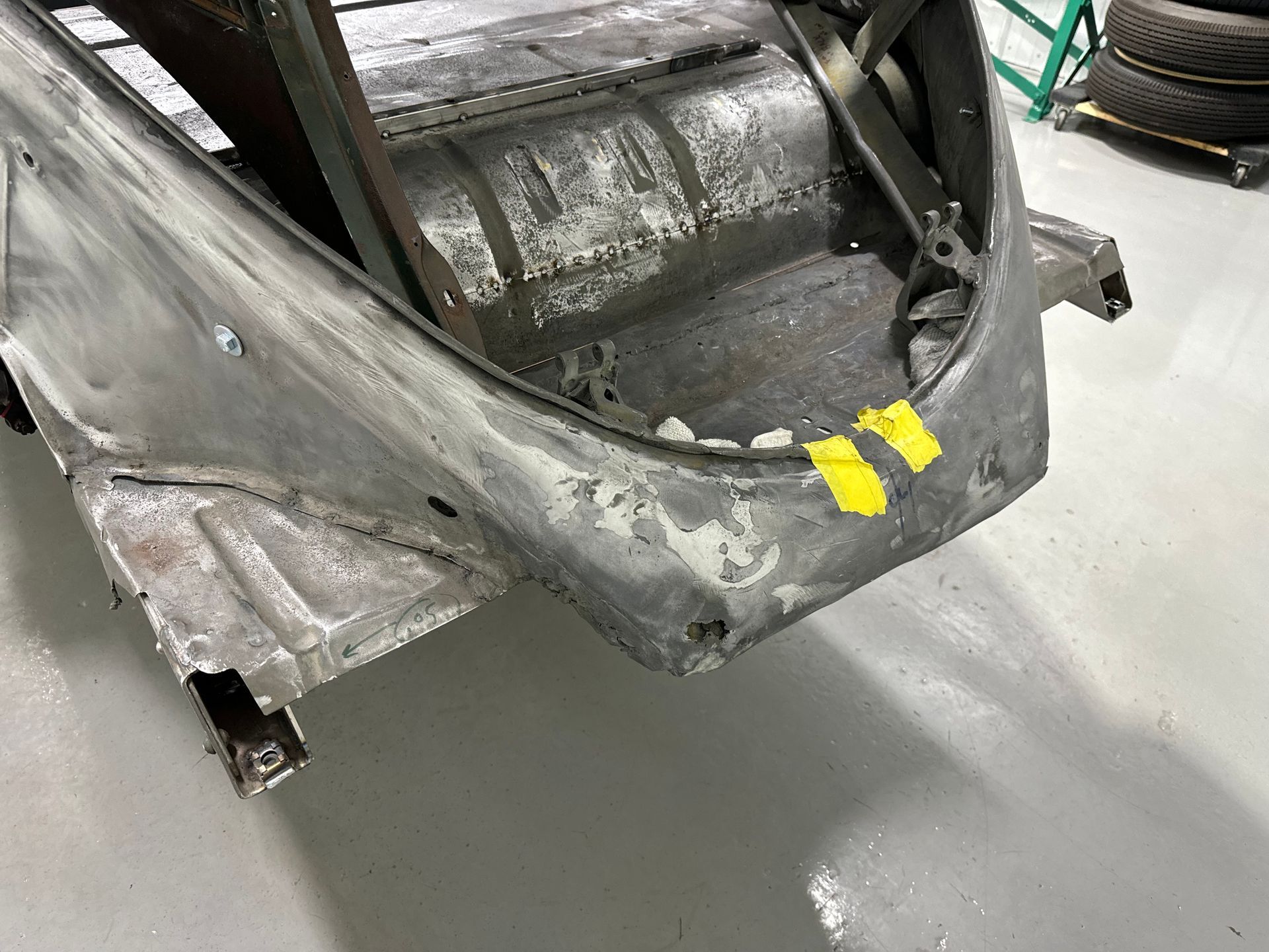 Damaged gray car body panel with yellow tape in a workshop floor area