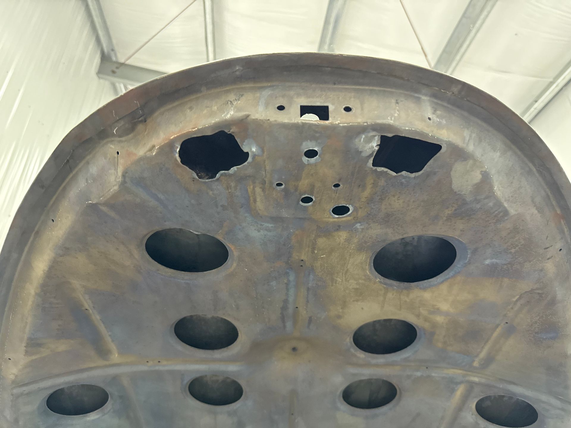 Close-up of a weathered metal surface with multiple oval and irregular cutouts beneath a curved edge