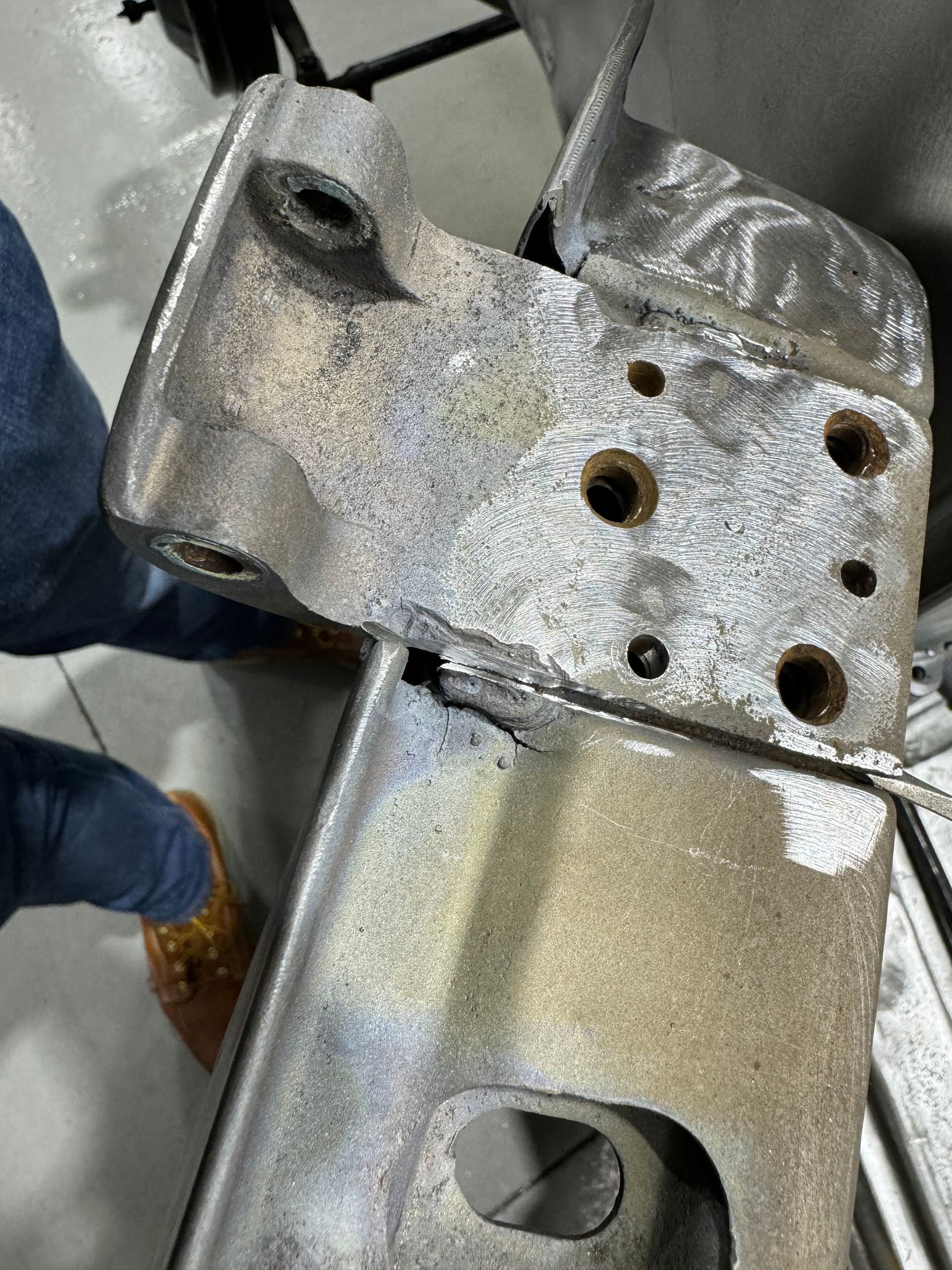 Close-up of a metal bracket with multiple bolt holes, held by a gloved hand.