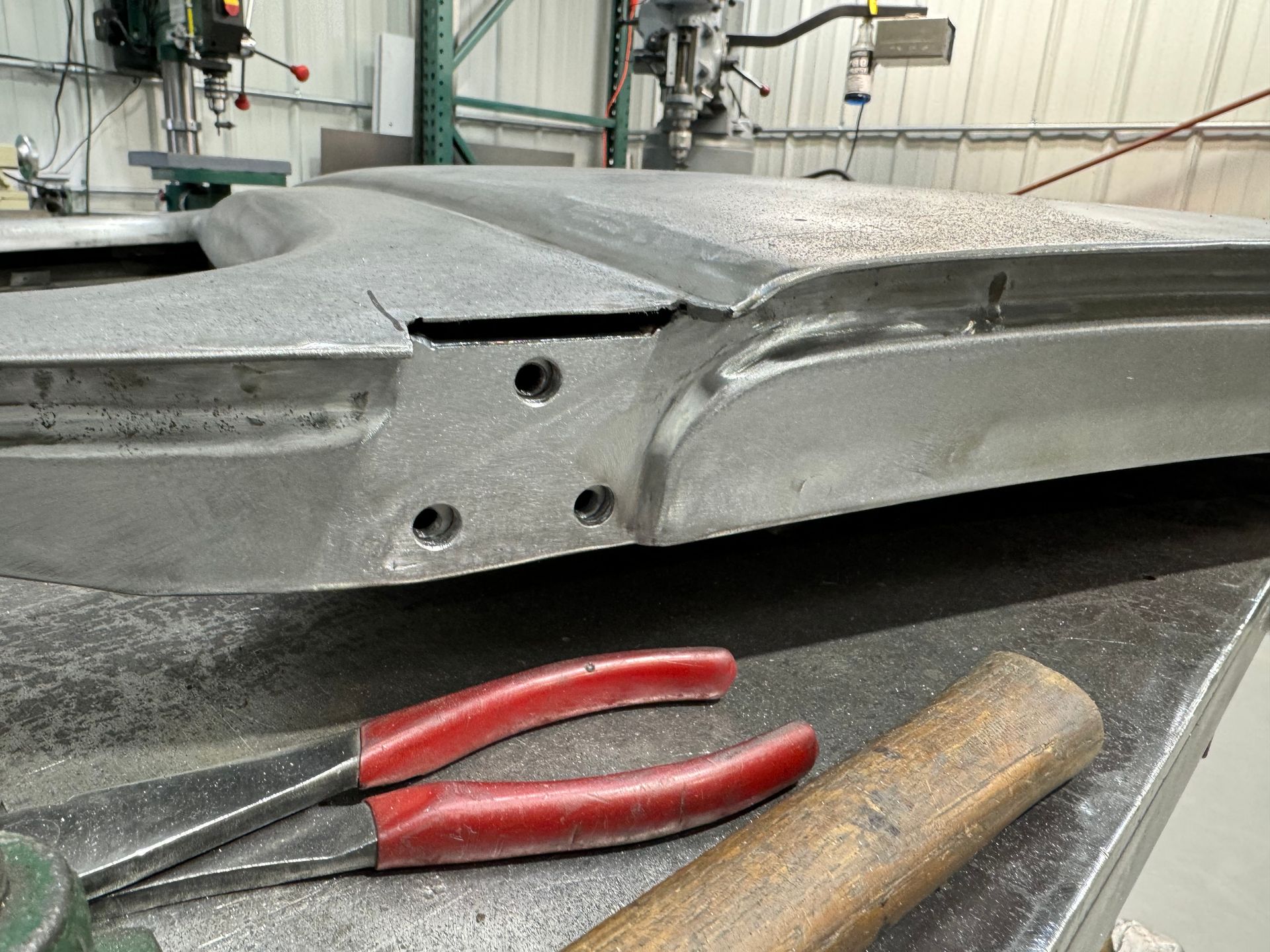 Damaged metal frame on a workbench with red-handled pliers and a wooden-handled tool in front