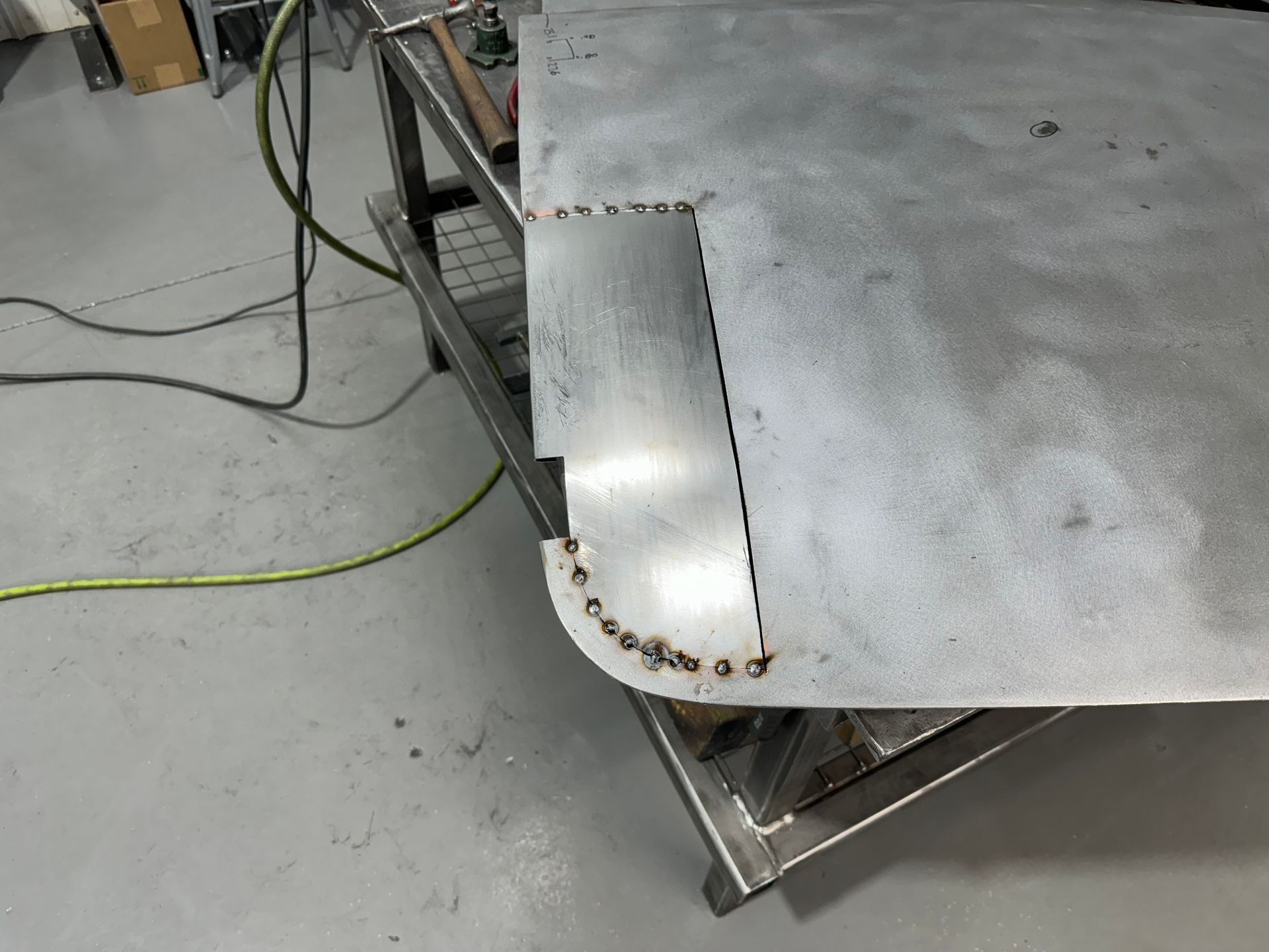 Metal machine corner with bolted plate on a gray workshop floor, with a cable nearby