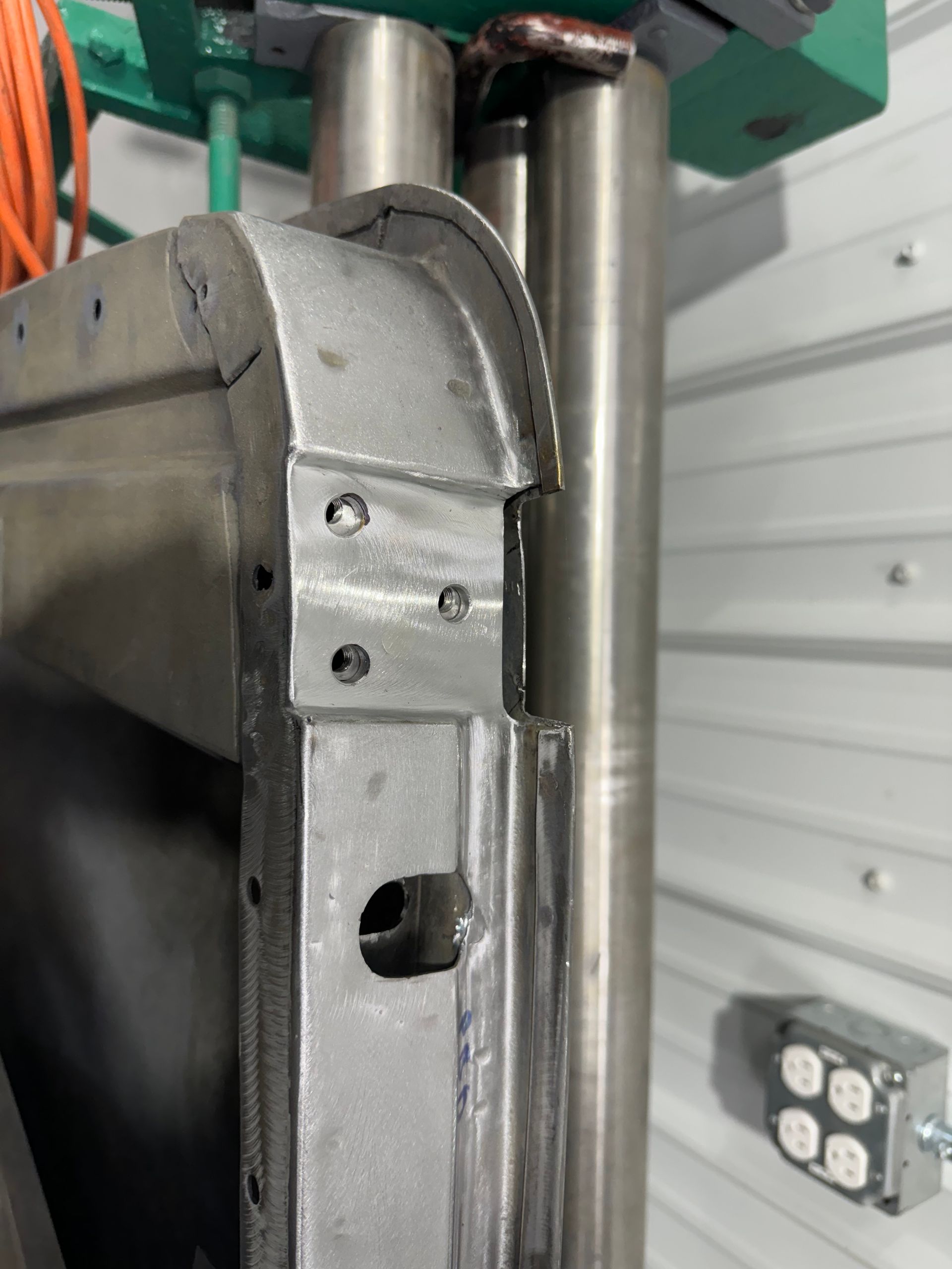 Close-up of a gray metal machine frame beside a polished vertical rod and orange cables.