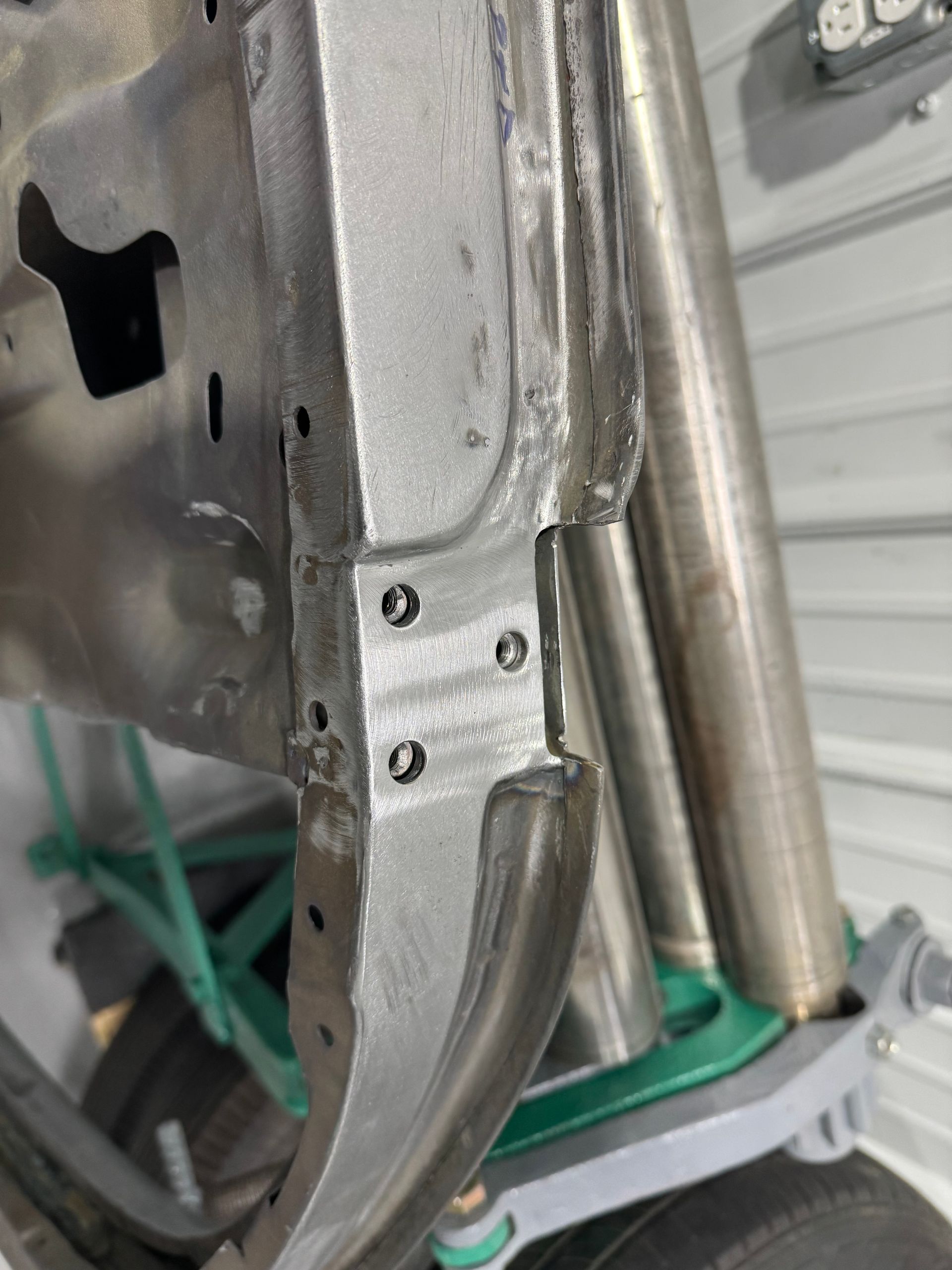 Close-up of a metal chassis corner with riveted brackets and curved tubing in a workshop setting