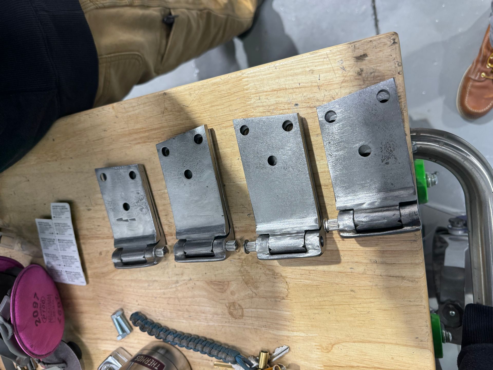 Metal hinges and small hardware parts arranged on a wooden board beside tools.