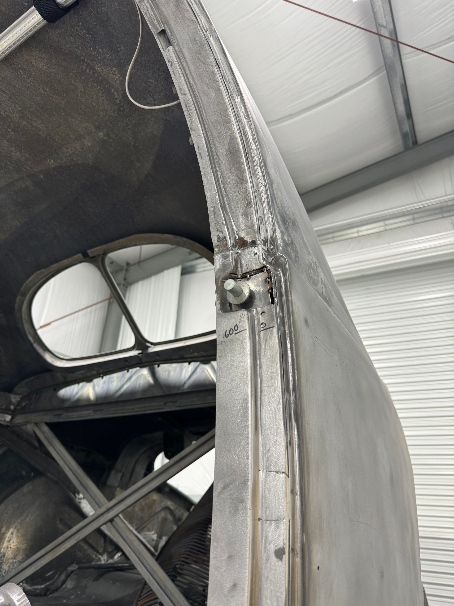 Close-up of a damaged metal aircraft frame with torn skin and exposed structure inside a hangar