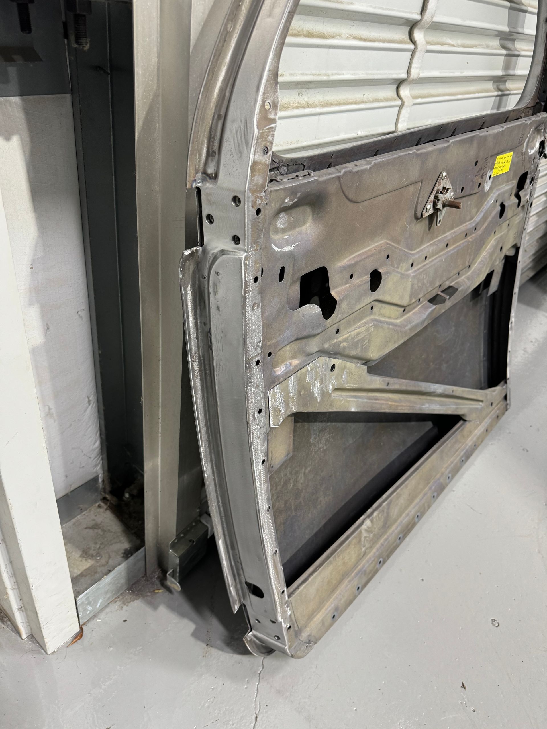 Damaged industrial metal door with a large hole, leaning open in a gray interior space