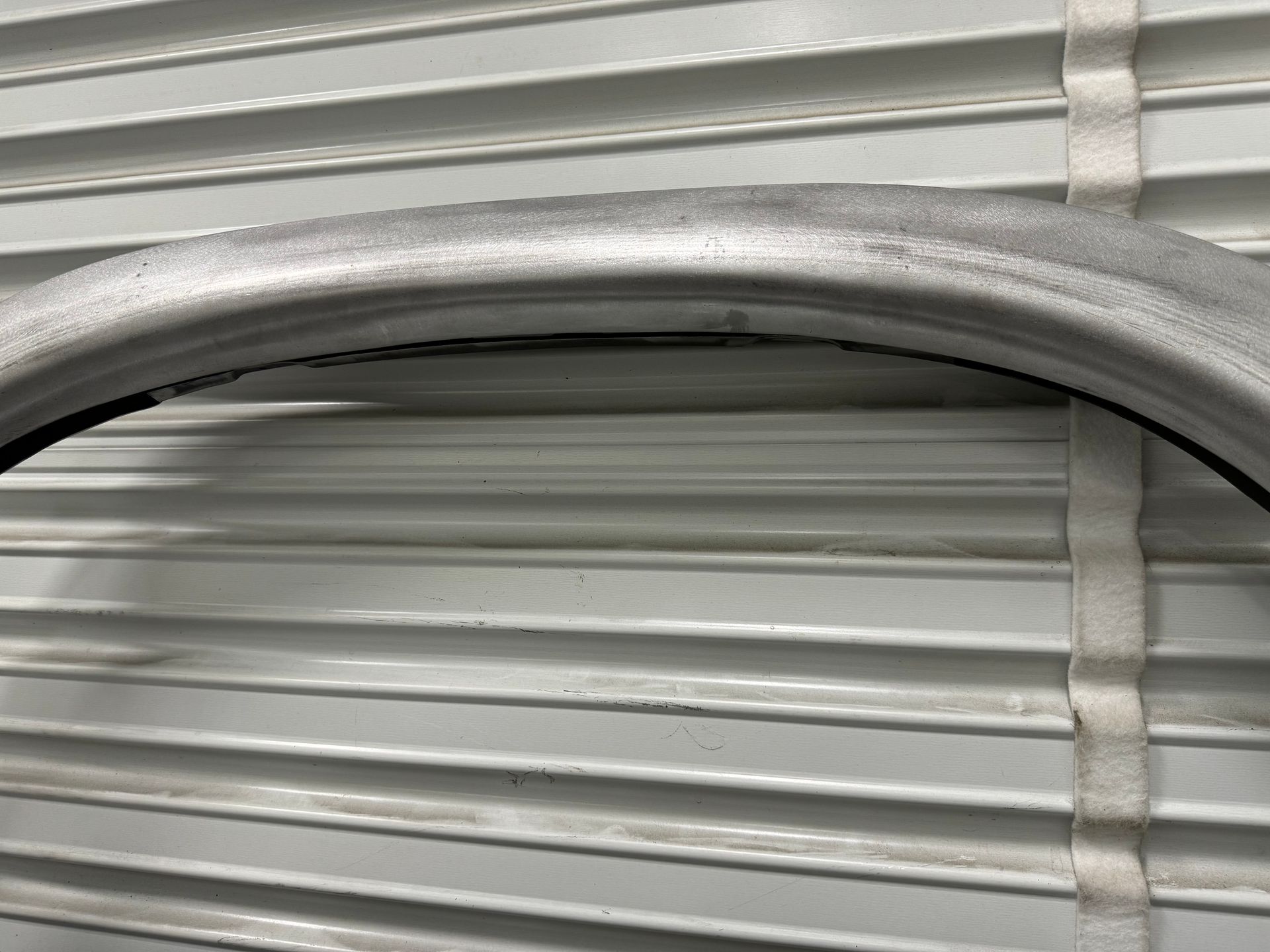 Close-up of a silver metal arch against a light gray corrugated background.