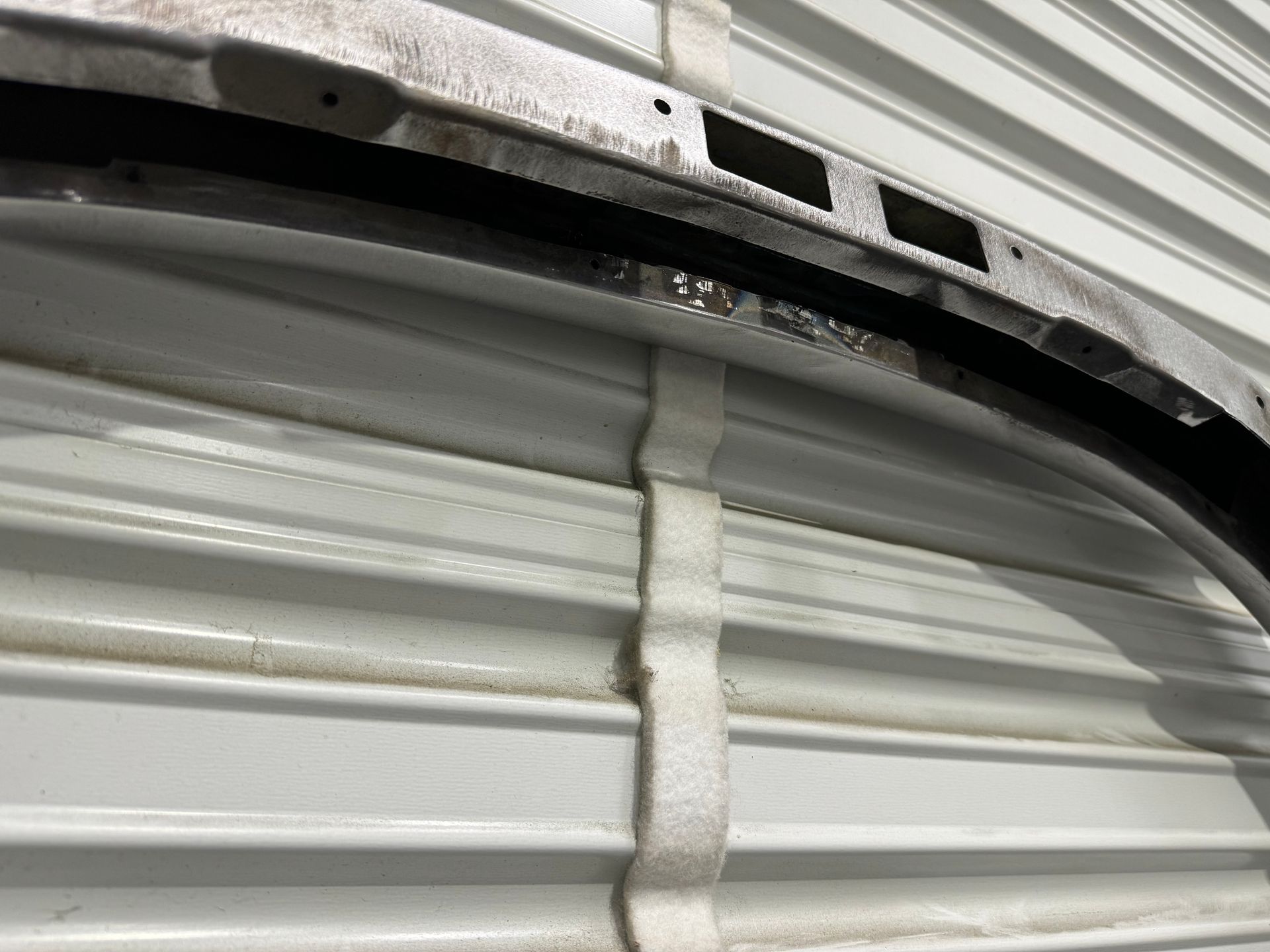 Close-up of a corrugated metal garage door with a strap and visible wear along the top edge