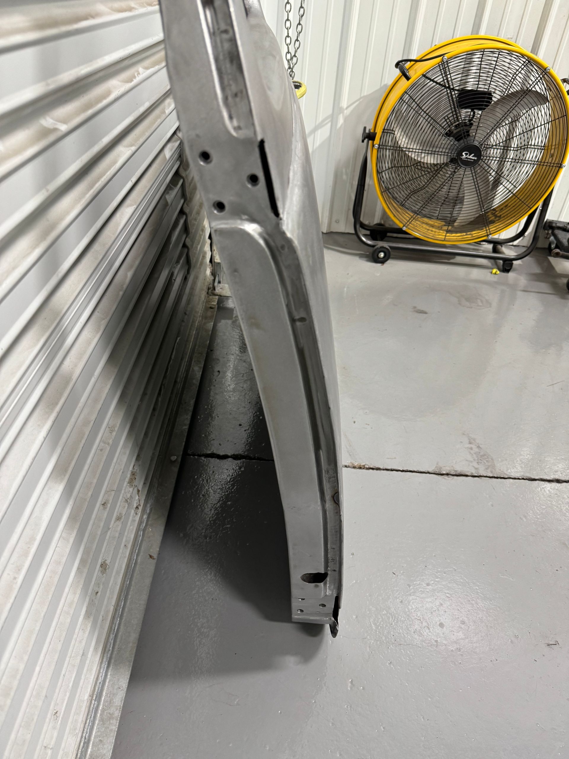 Bent metal panel leaning against a wall beside a yellow floor fan in a storage area