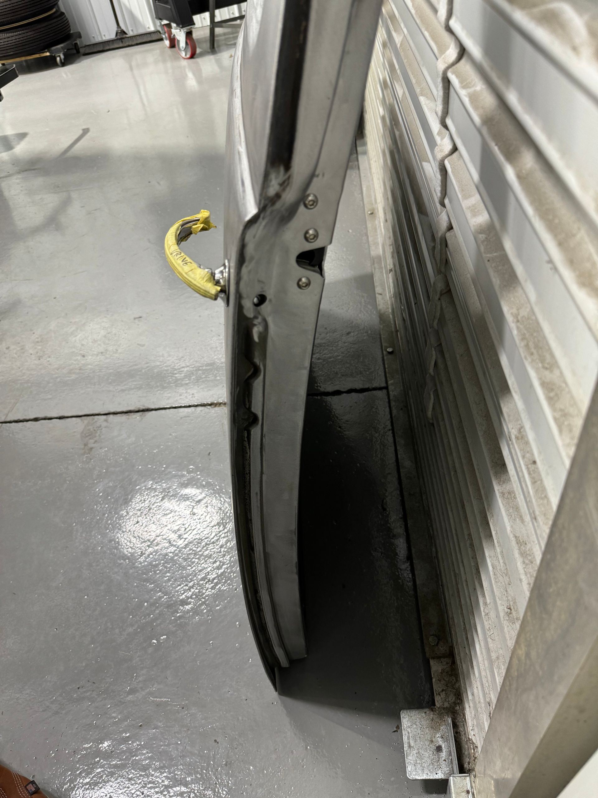 Bent metal frame leaning against a wall beside a wet concrete floor and yellow hose loop