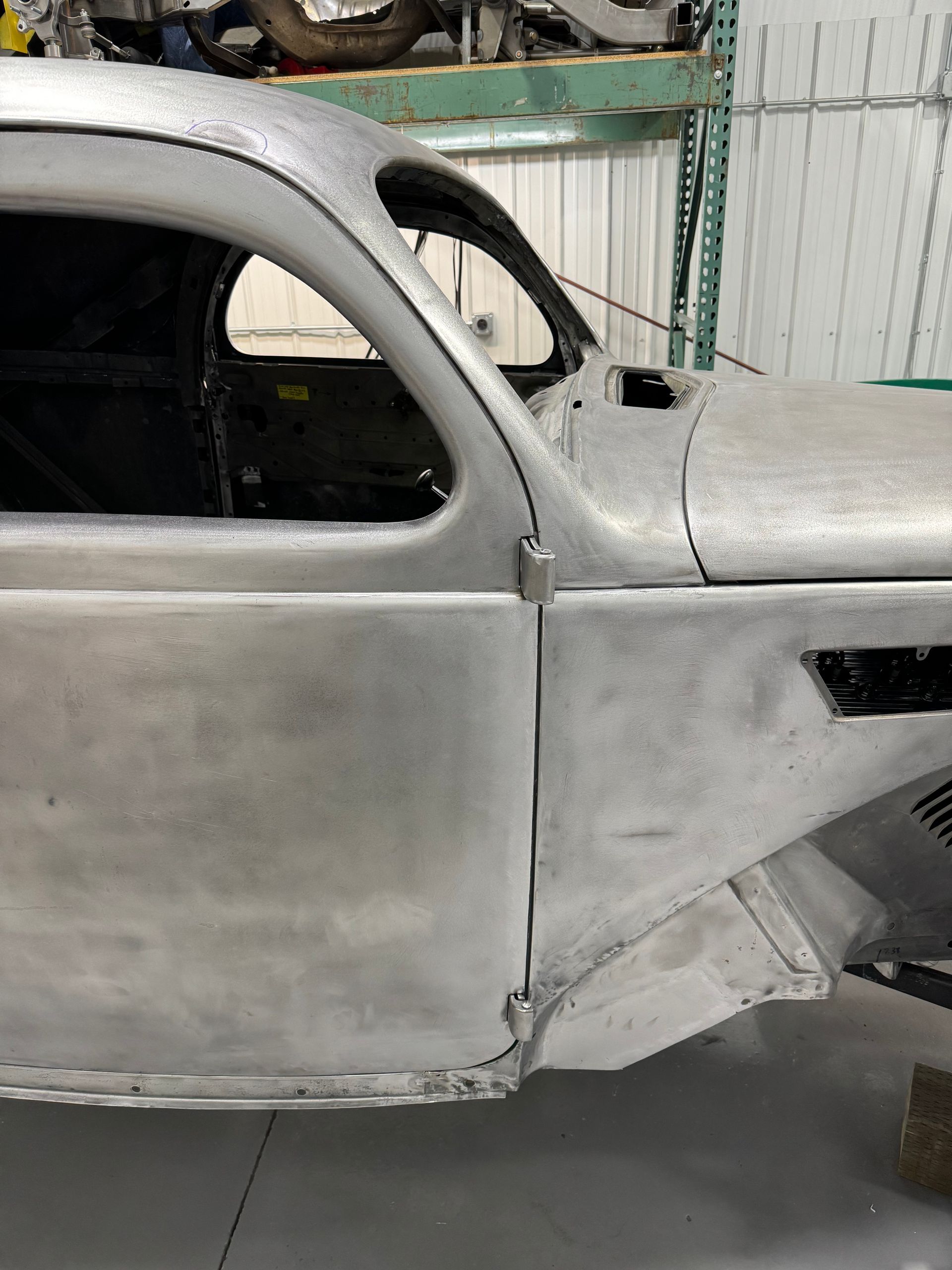 Primered vintage car body in a workshop, side view with door and front fender visible.