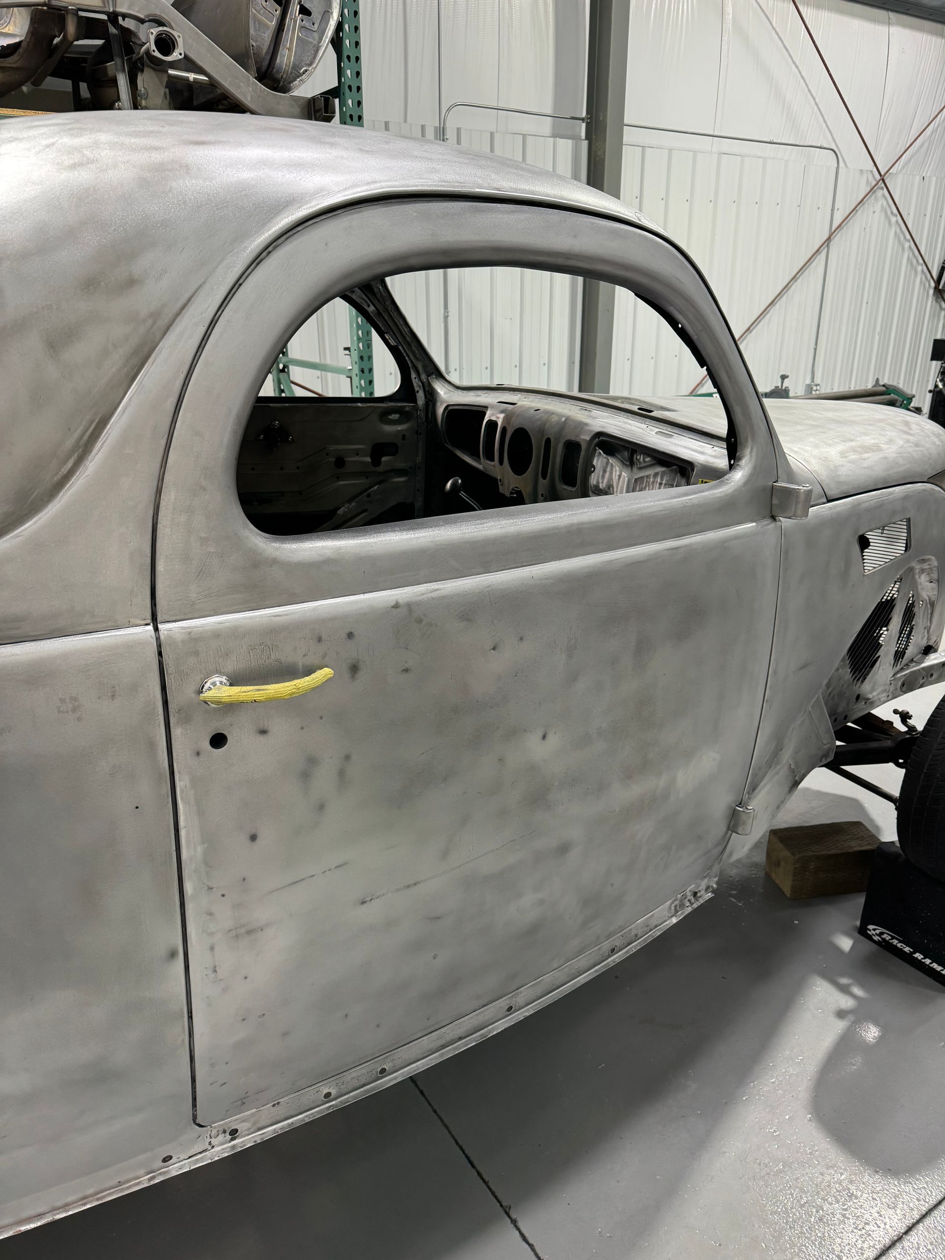 Gray classic car body shell in a workshop, stripped for restoration, with primer coating and open window frame