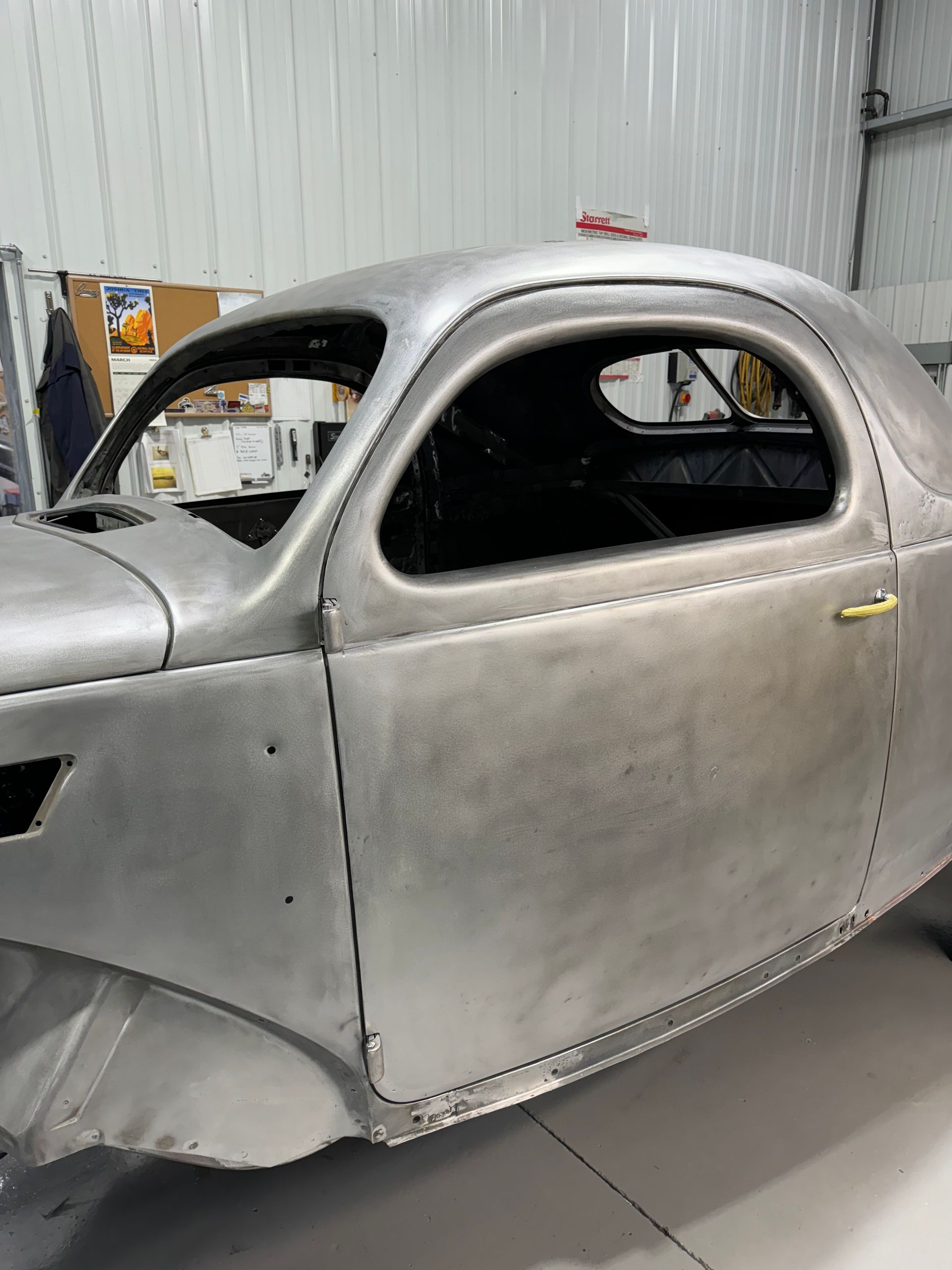 Bare metal vintage car body shell in a workshop, partially restored and unpainted