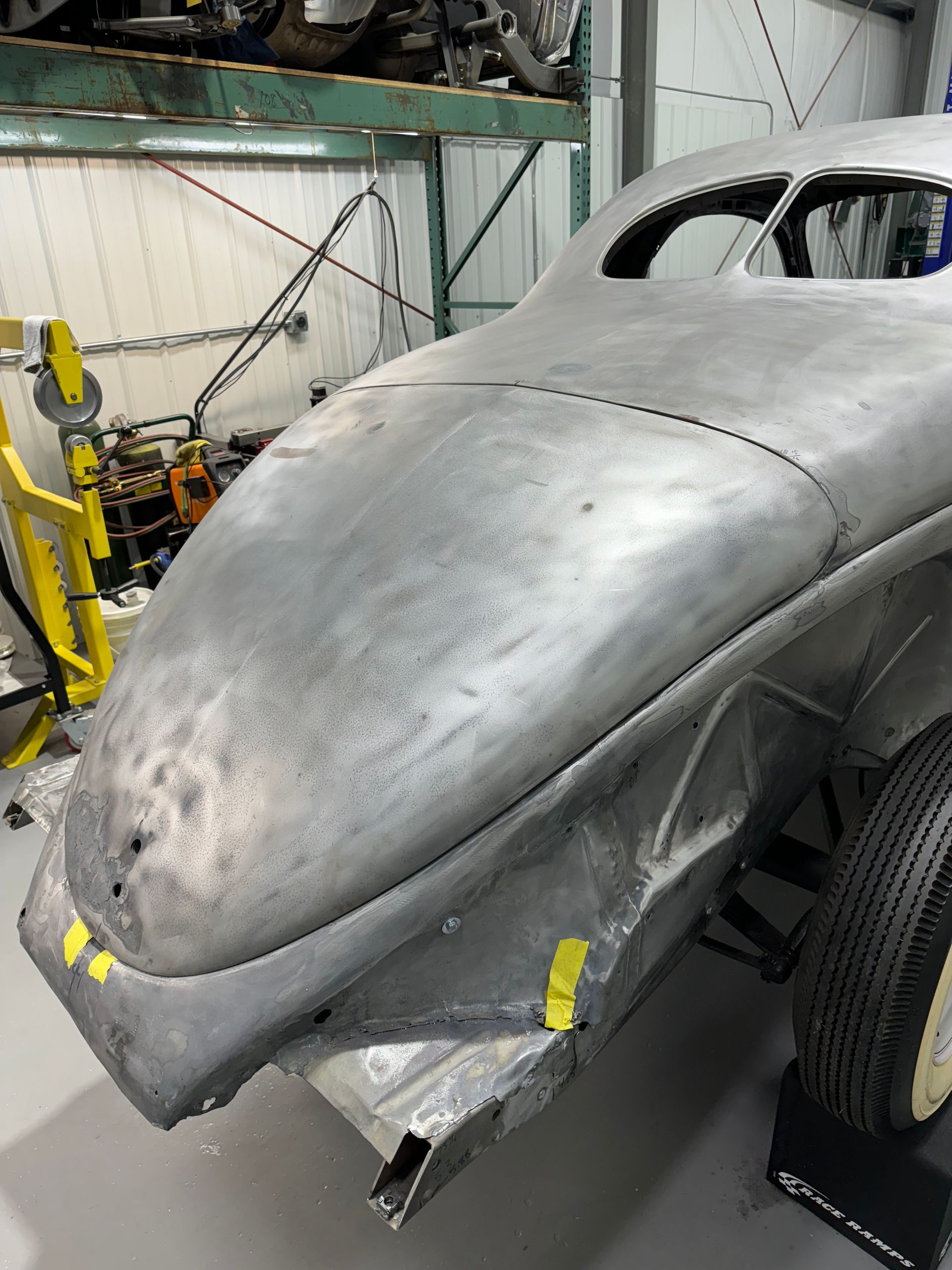 Partially restored silver car body in a workshop, with front bumper and hood removed
