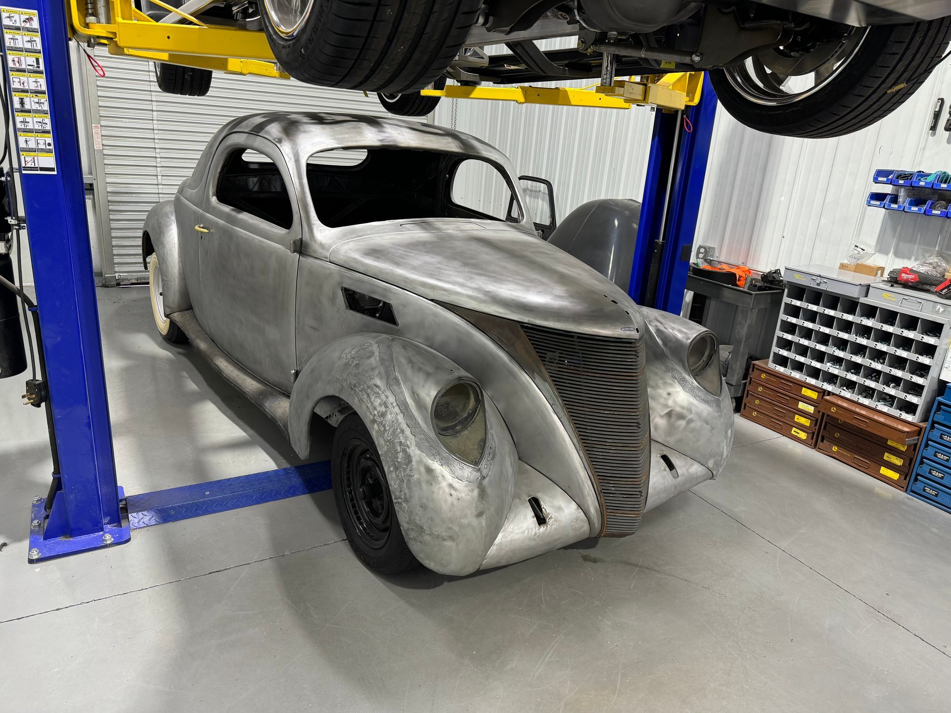 Silver vintage hot rod under repair on a lift in an auto shop