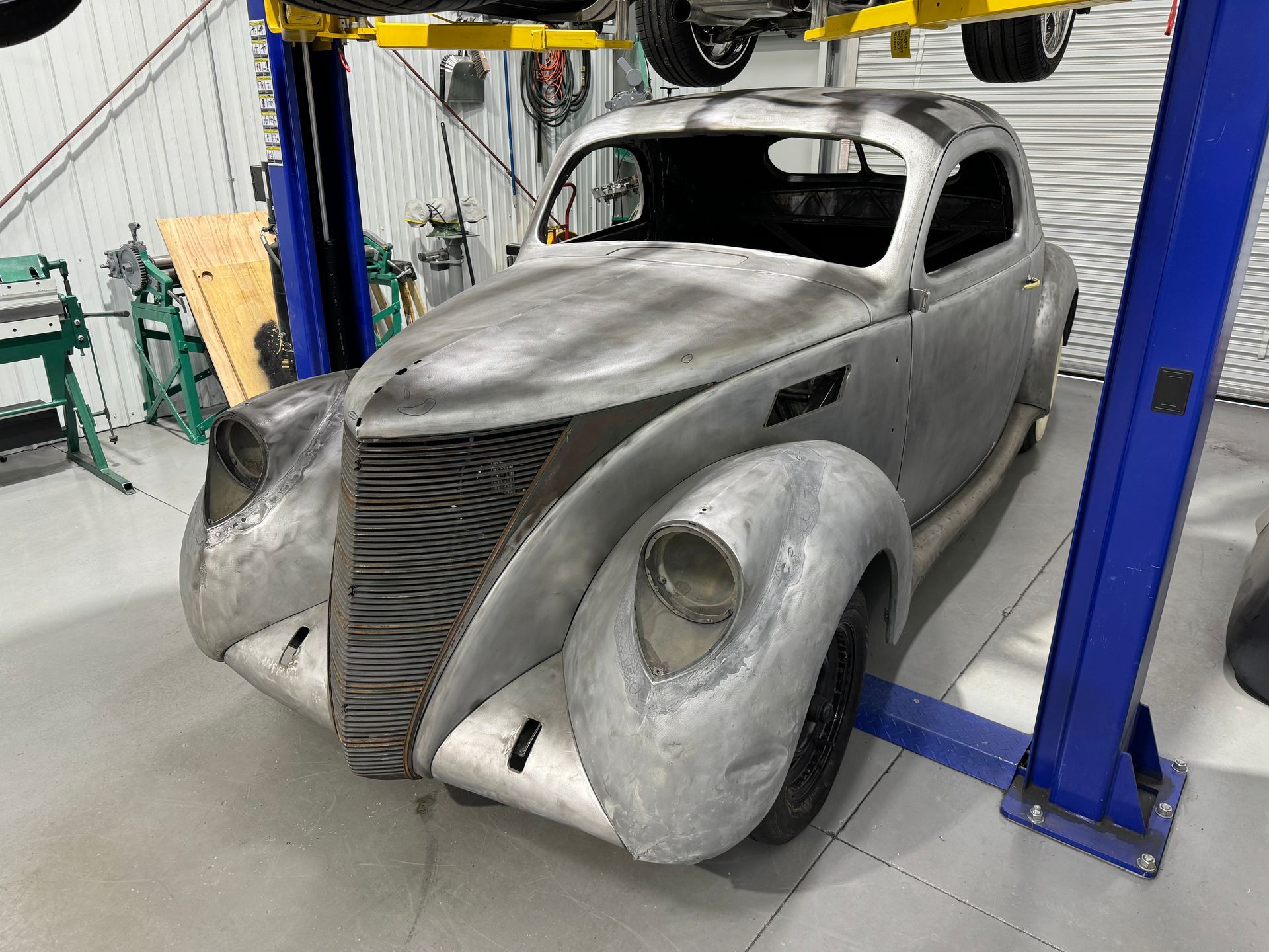 Vintage car body in gray primer on a lift in an auto shop