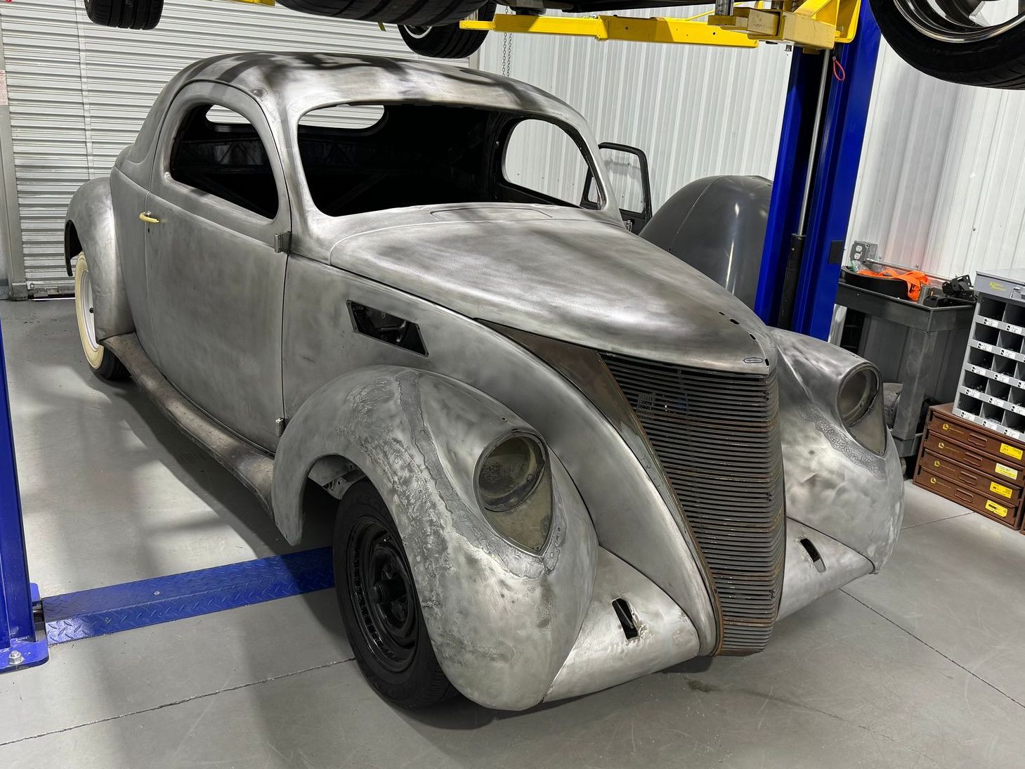 Silver vintage car body in an auto shop, raised on a lift with unfinished panels and primer coating