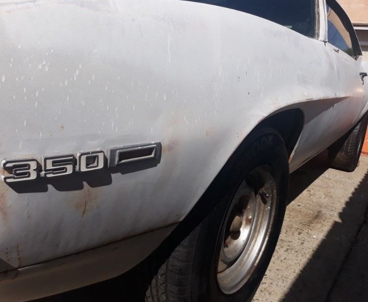Close-up of a white classic car’s rear side, showing the 350 badge and wheel.