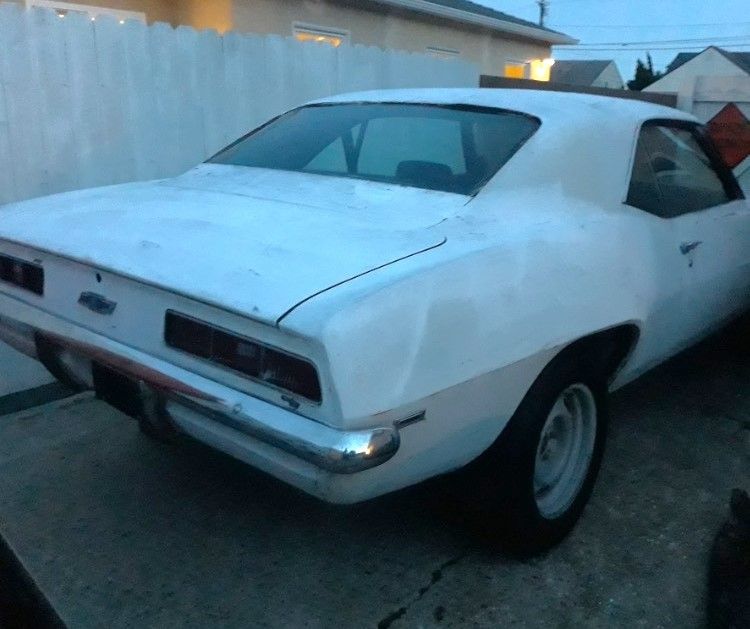 White classic muscle car parked in a driveway beside a white fence at dusk