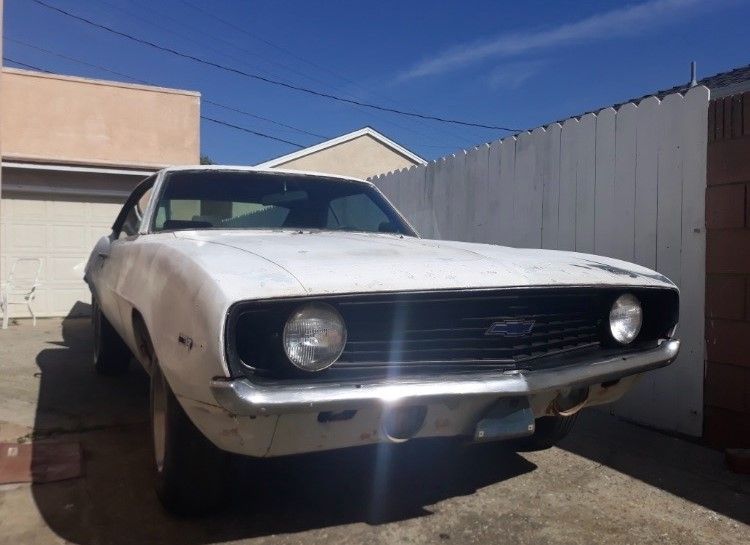 White classic car parked in a driveway beside a fence and garage
