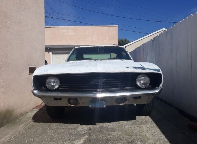 Front view of a white classic car parked in a narrow driveway between two walls.