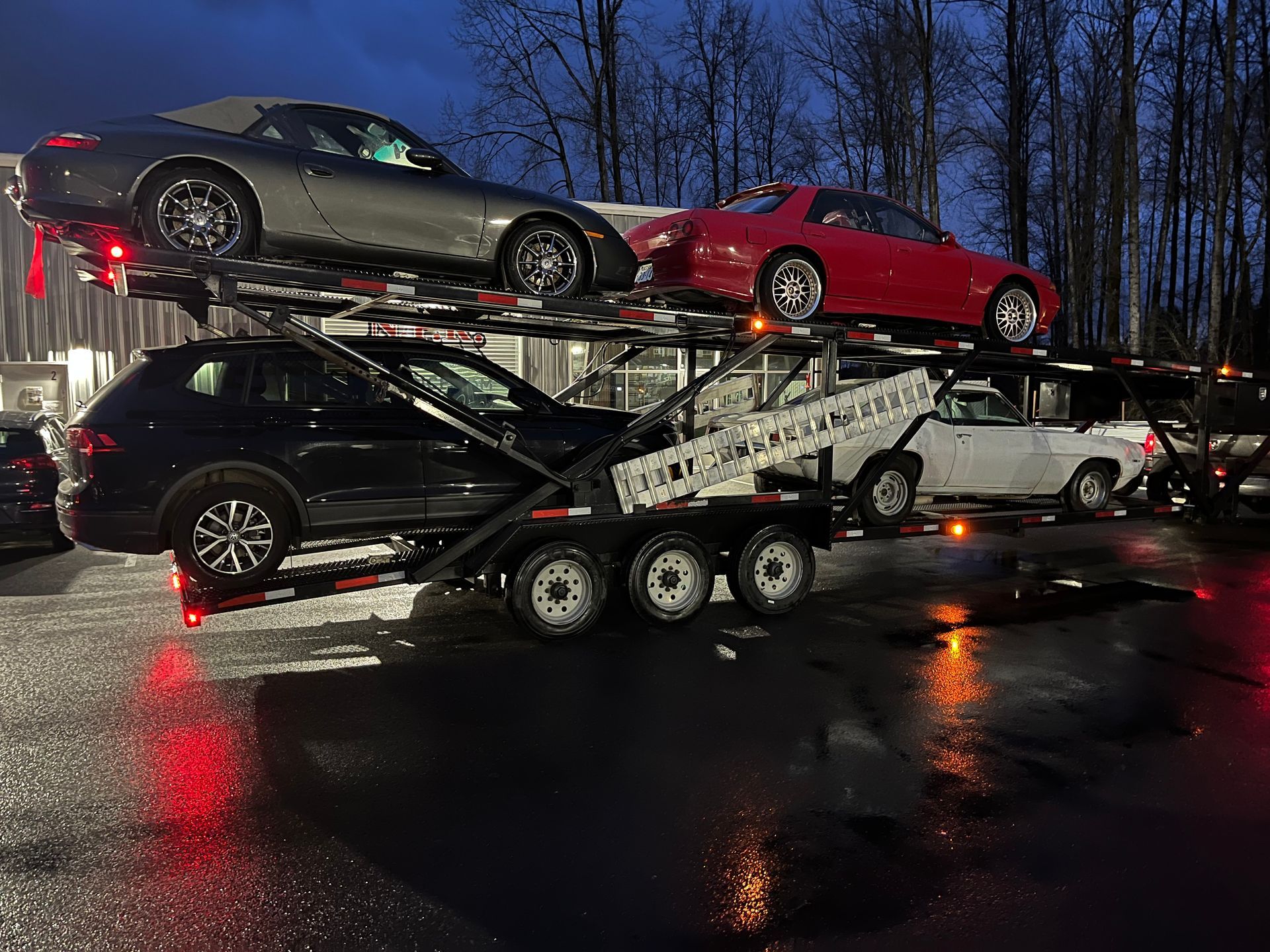 Car carrier truck loaded with several cars on a wet street at night, reflecting lights on the pavement