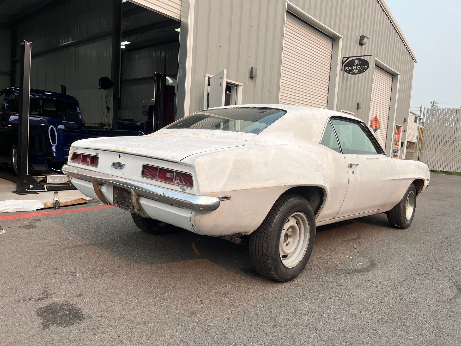 White classic muscle car parked outside an auto shop with garage doors open