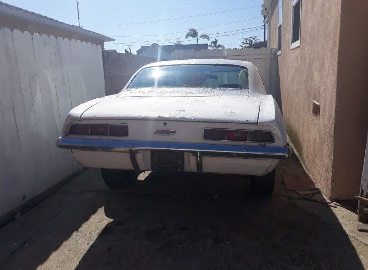 White classic car parked in a narrow driveway between two walls, rear view under bright sunlight