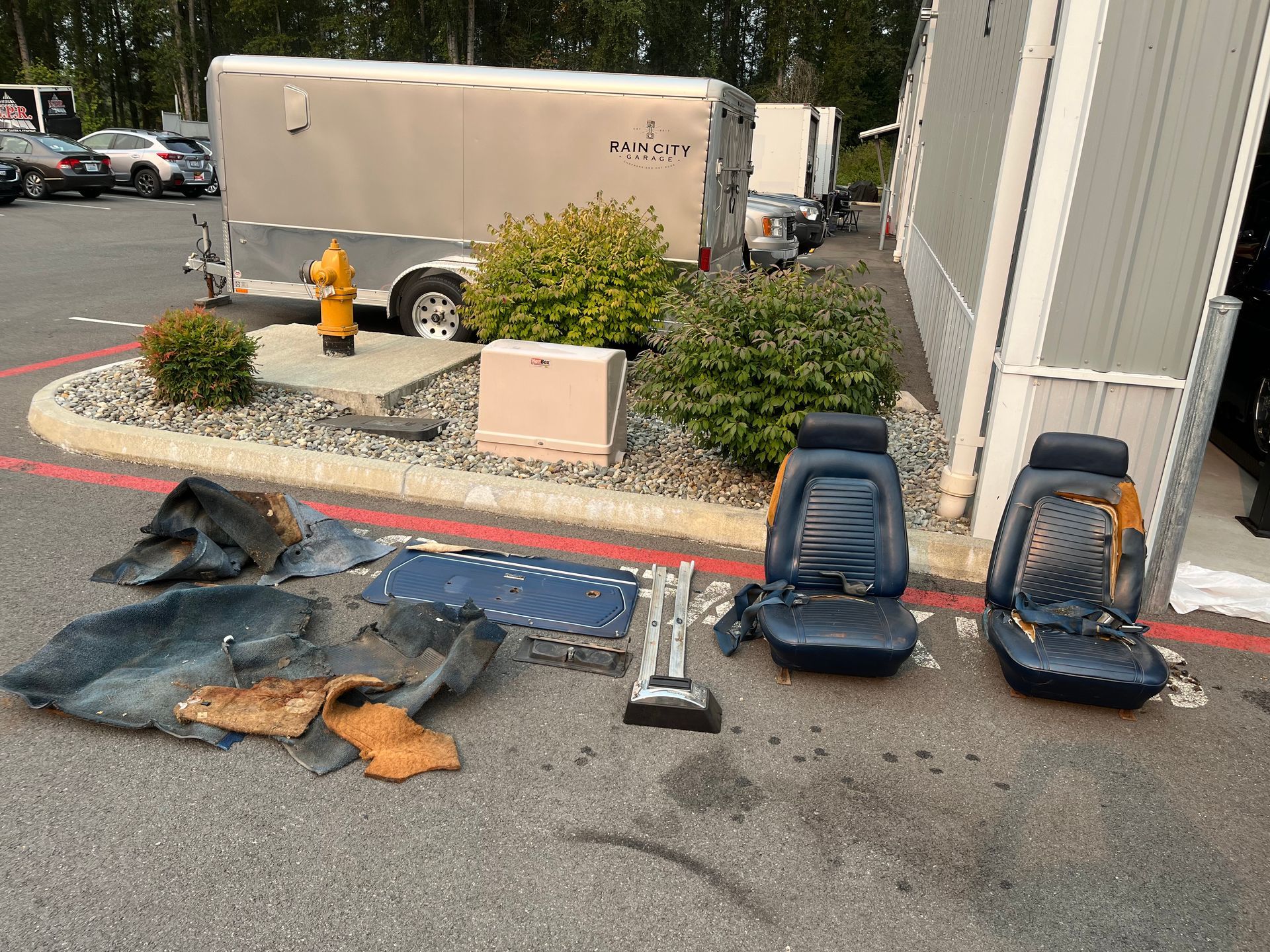 Two seat covers, mats, and car parts laid out on pavement beside a building and planter.