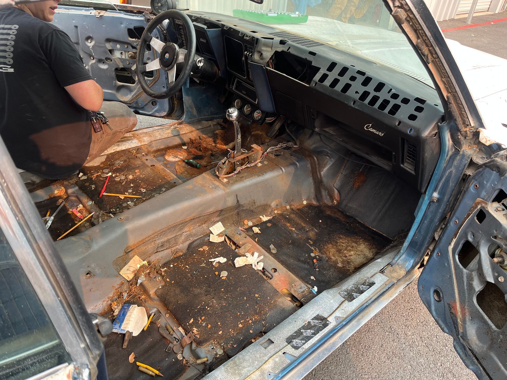 Burned car interior with charred seats and debris, door open, person leaning inside