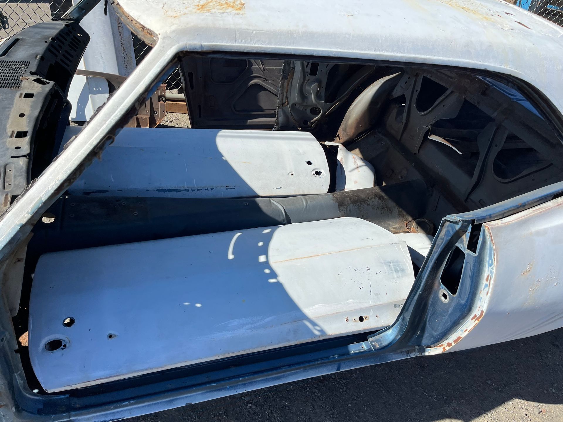 Stripped car interior with blue panels and exposed metal frame in a garage or yard