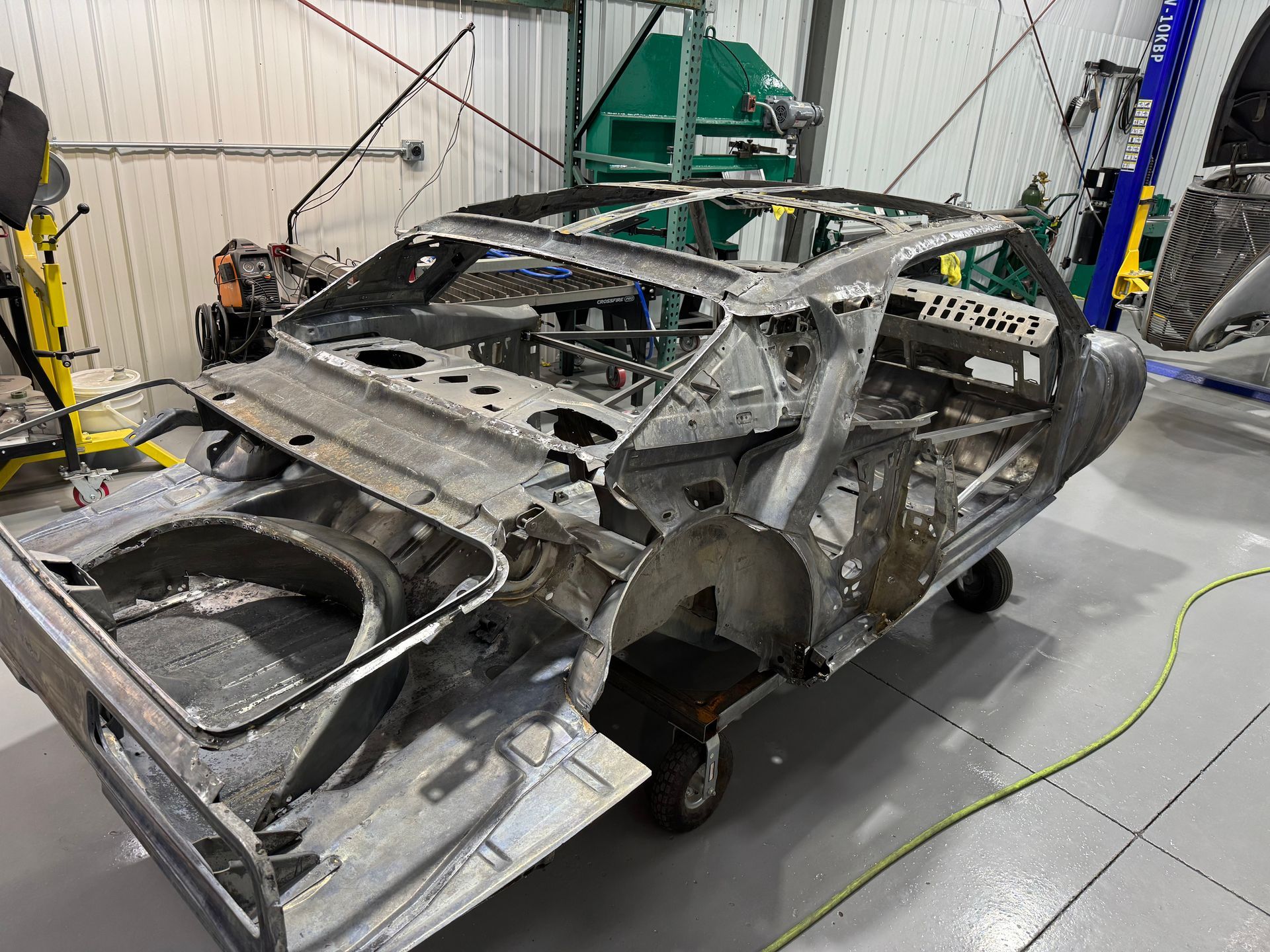 Stripped car body shell in an auto workshop, exposed metal frame on a floor stand